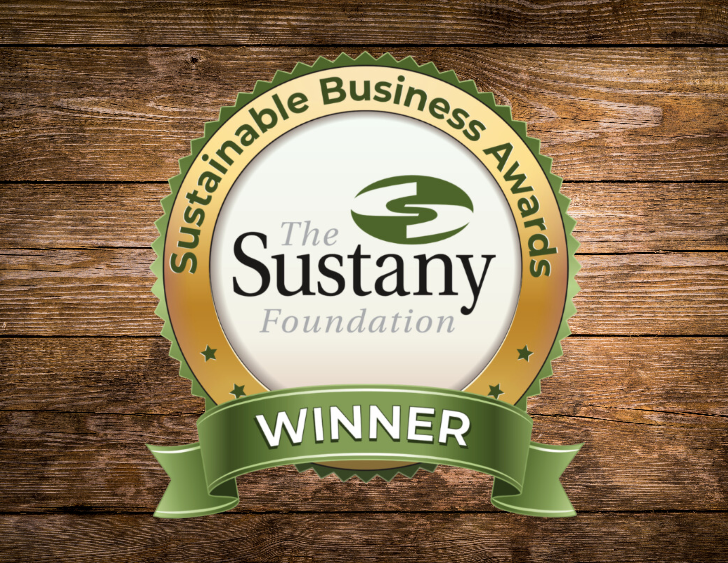 Award badge with the text "The Sustany Foundation" in the center, surrounded by the words "Sustainable Business Awards" and a green ribbon with "WINNER" written on it, on a wooden background.