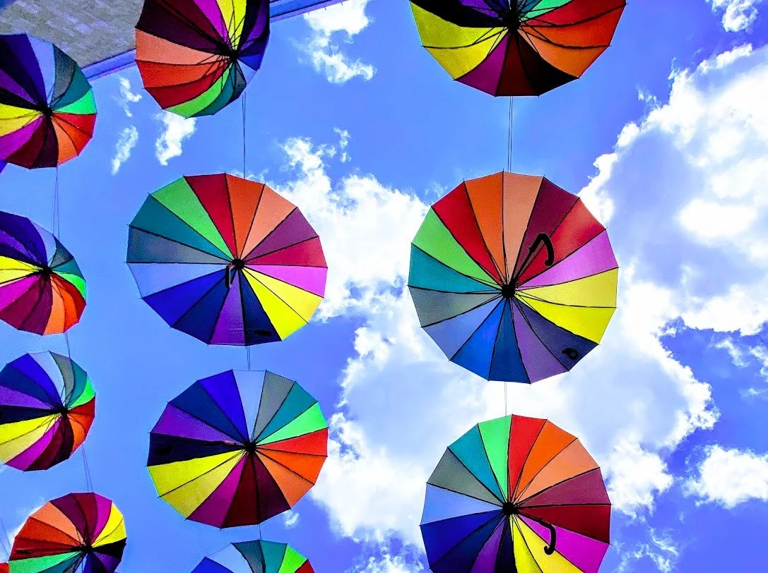 Colorful umbrellas hanging upside down against a bright blue sky with scattered white clouds.
