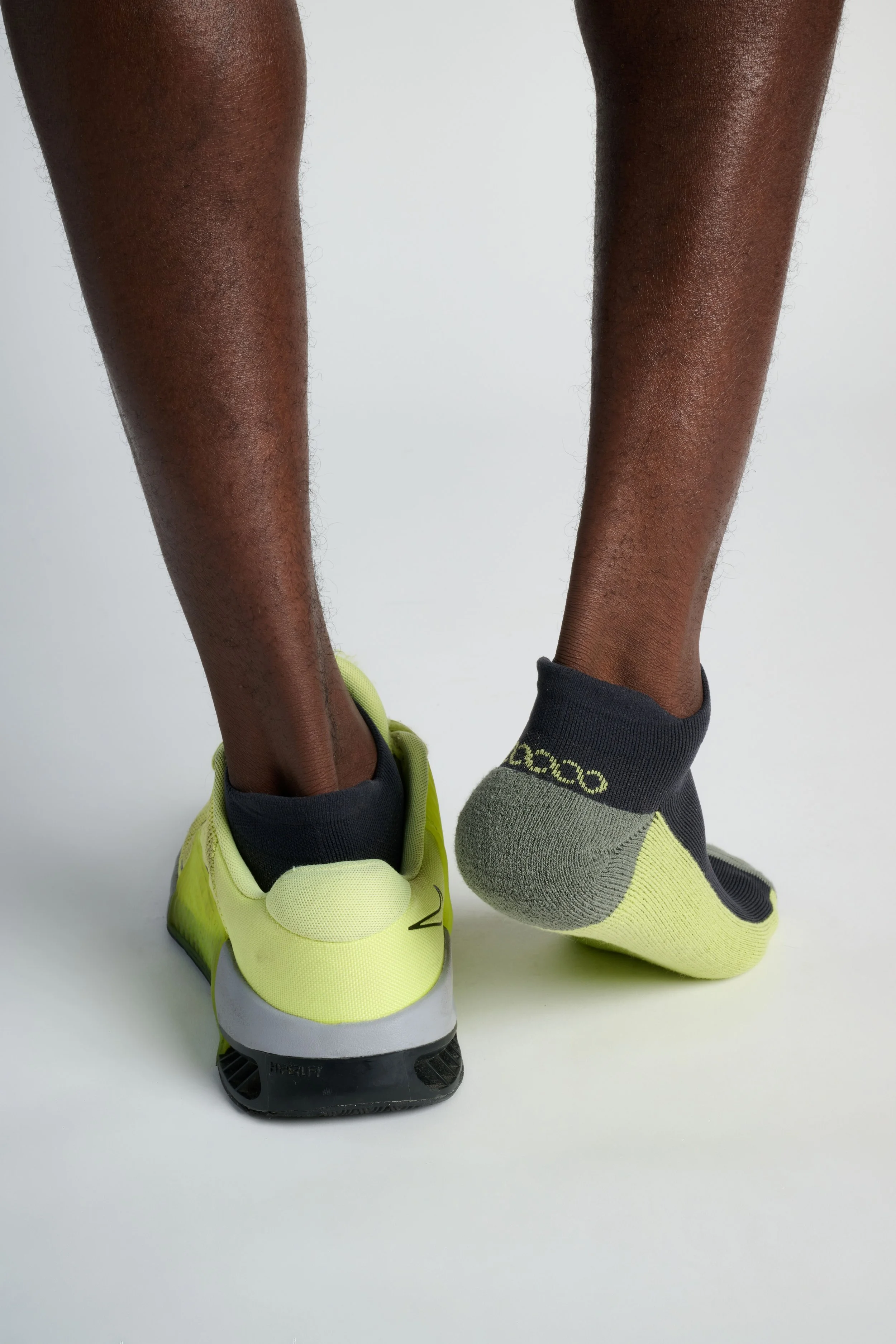 Man wearing multicolor low-cut performance running socks in black, blue, and green with cushioned support and breathable fabric for training and everyday wear.