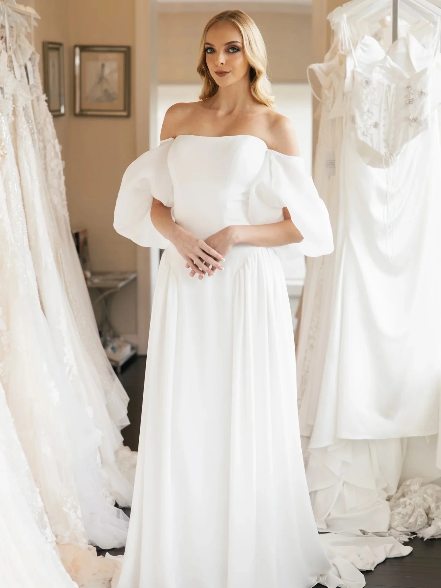 HA2987 is modern minimalism with a romantic edge. Crafted in sleek crepe, this gown pairs a clean, structured bodice with dramatic off-the-shoulder puff sleeves for a sculptural yet soft silhouette. Effortless draping through the skirt adds movement 