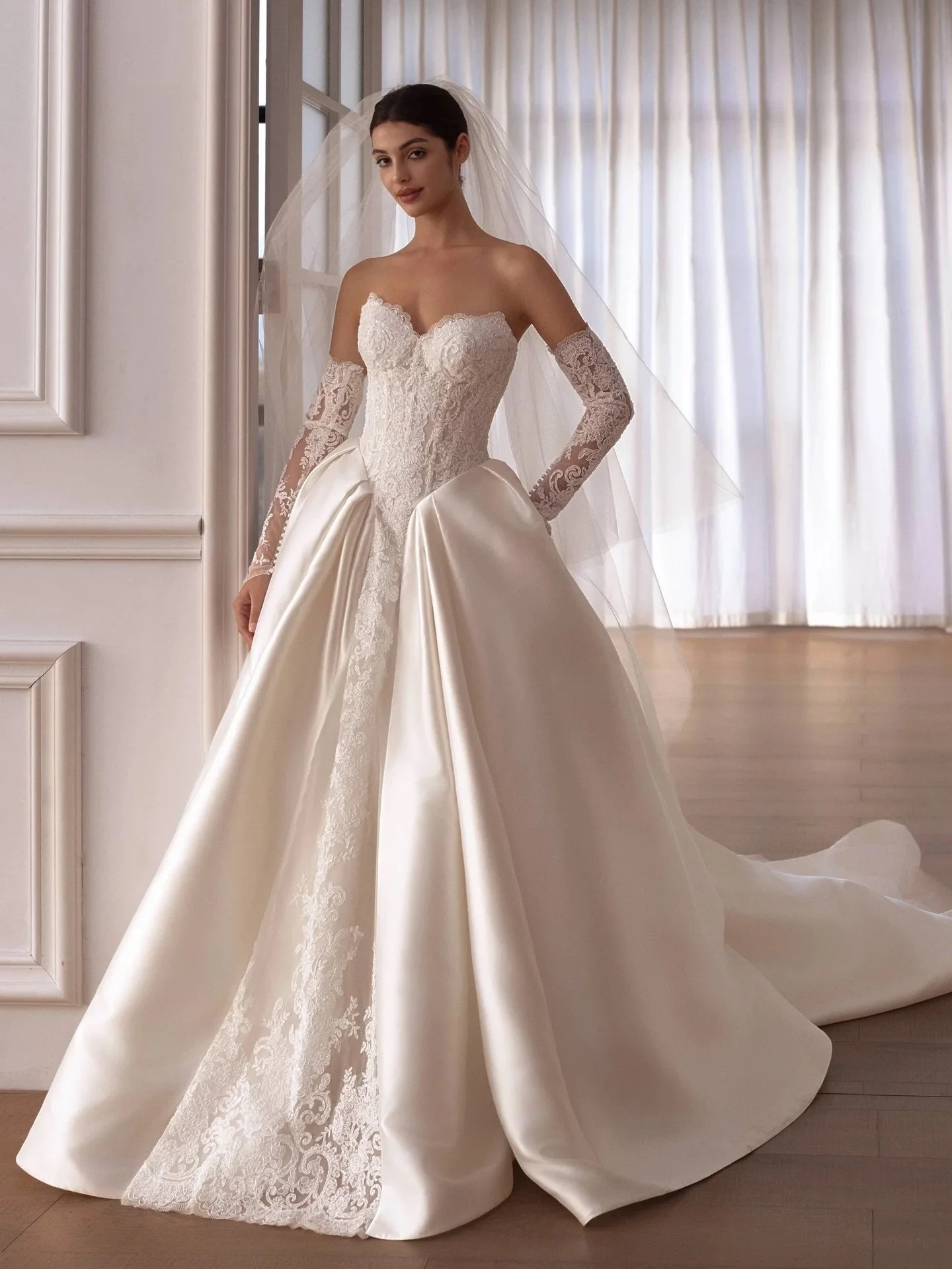 A cat-eye ballgown defined by lace and Mikado fabric-blocking, offering an elegant, design-forward statement with a forgiving silhouette, finished with detachable lace sleeves for styling versatility.