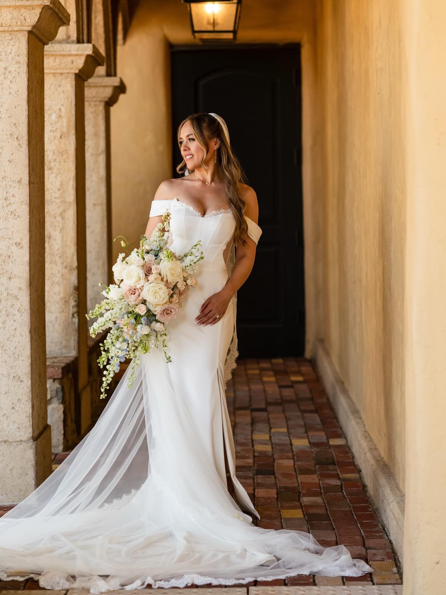 Talia looked effortlessly timeless in a gown that balanced clean structure with the softest romantic details. The sculpted corset bodice, delicate lace trim, and off-the-shoulder neckline created such an elegant silhouette, while the flowing train ad