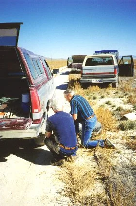 8. Made 10/18/97 , just east of Lucin, UT. Al Mulder Gets a Flat. Photograph by Steve Berlin. No sooner had we started along the old roadbed when crackling over the CB came the message, "Flat tire!" We'd been warned about the possibility that old spikes from the railway could still be lying about and could puncture a tire with ease, but we weren't prepared for how many flat tires we would have and just how devastating most of the punctures were. Before the day was out our group of 15 vehicles had experienced 8 flats! The damage was so great that in most cases treads and sidewalls were shredded making repair of the tires impossible. In this picture Al Mulder goes to work after stopping for someone else's flat and finding one of his own tires was leaking too. Al's was the gentlest of the day's flats - most were blowouts.