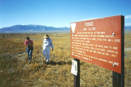 11. Made 10/18/97 at Terrace, UT about 25 miles east of Lucin, UT. Terrace. Photograph by Steve Berlin. Looking approximately north. Terrace is west of Promontory Summit where the Central Pacific rails from the west joined the Union Pacific rails from the east. It was the maintenance and repair headquarters for the CPRR for its Salt Lake Division which encompassed the road from Wells, Nevada to Ogden, Utah. Though railroad use ended by about 1910, in its heyday Terrace not only boasted extensive railroad facilities including a full roundhouse but perhaps 1,000 inhabitants. Nine-tenths of the workers who built the CPRR were Chinese and estimates run as high as 500 such residents of Terrace at one time. No structures remain at the site and like all the railroad installations along the grade Terrace has been extensively looted by bottle and artifact hunters. Deep holes dug by these vandals pit the landscape in every direction. Although artifacts remain, with the area now under active historic preservation management by the BLM and with the involvement of a concerned public, such depredations have decreased considerably in recent years. The sign says: TERRACE - 1869 - CA, 1910, MILE 702.1 FROM SAN FRANCISCO; 1153 FROM OMAHA TERRACE BECAME A POPULATION CENTER FOR NW UTAH, SUPPORTING BUSINESSES, STORES, A SCHOOL, A WELLS FARGO OFFICE, A LIBRARY, A PUBLIC BATH, AND A JUSTICE OF THE PEACE (WHO ALSO RAN THE SALOON). BUSINESS BUILDINGS LINED A WIDE AVENUE NORTH OF THE TRACKS WHILE THE MORE SCATTERED RESIDENTIAL STRUCTURES WERE GENERALLY TO THE SOUTH. ALTHOUGH ALL WATER IN TOWN WAS PIPED IN, THERE WAS A NICE TOWN SQUARE AND TREE - LINED STREETS IN THE RESIDENTIAL AREA. WHEN THE LUCIN CUTOFF WAS COMPLETED IN 1904 AND THE MAINTENANCE SHOPS WERE MOVED TO CARLIN, NV, THE TOWN BEGAN TO DIE.