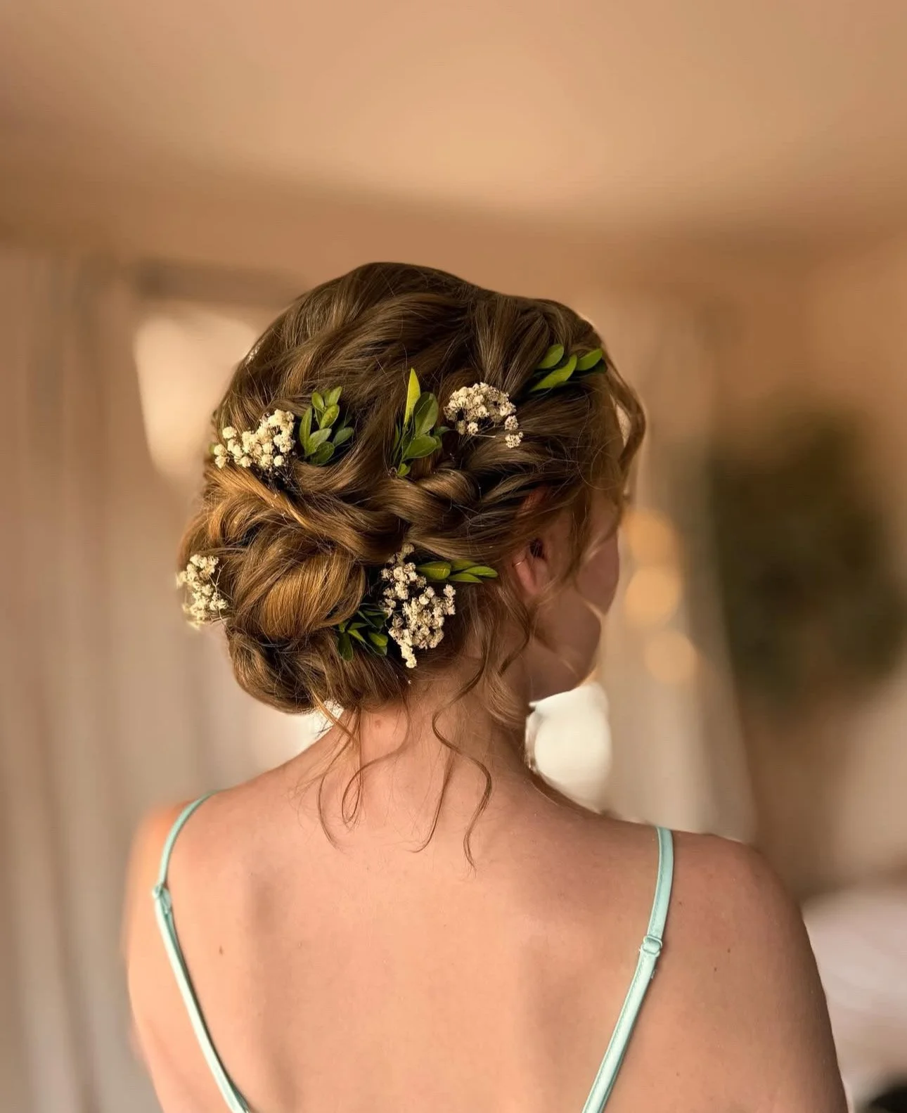 Wedding hair styled in an elegant updo with pearls and greenery woven into the design