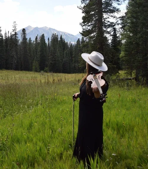 Elopement ceremony ideas illustrated by a violinist standing in a peaceful mountainous meadow