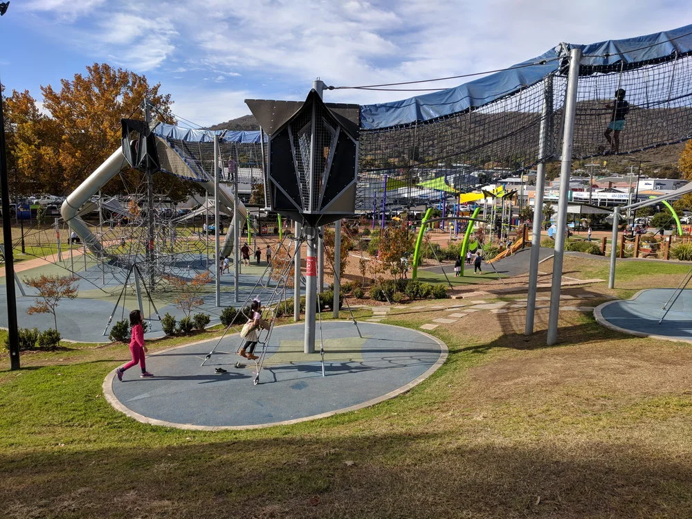 Suspended walking bridge with safety net and shade cloth leading to large slides