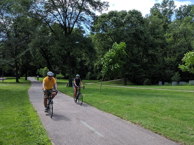 Cycling path with walking path in background leading to footbridge over Minnehaha Creek with lots of vegetation along creek banks