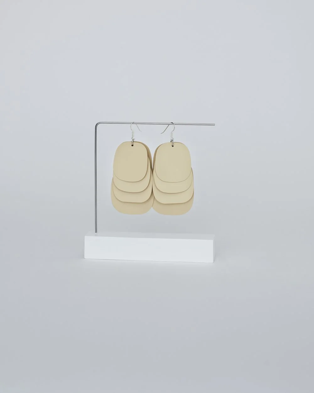 A pair of beige multi-layered statement earrings with sterling silver hooks. Each lightweight earring features multiple overlapping oval shapes.