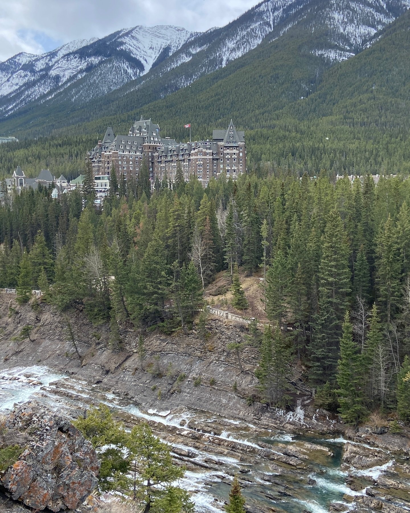 The iconic view of the Fairmont Banff Springs Hotel from Surprise Corner with Sulphur Mountain in the background and the Bow Falls in the foreground