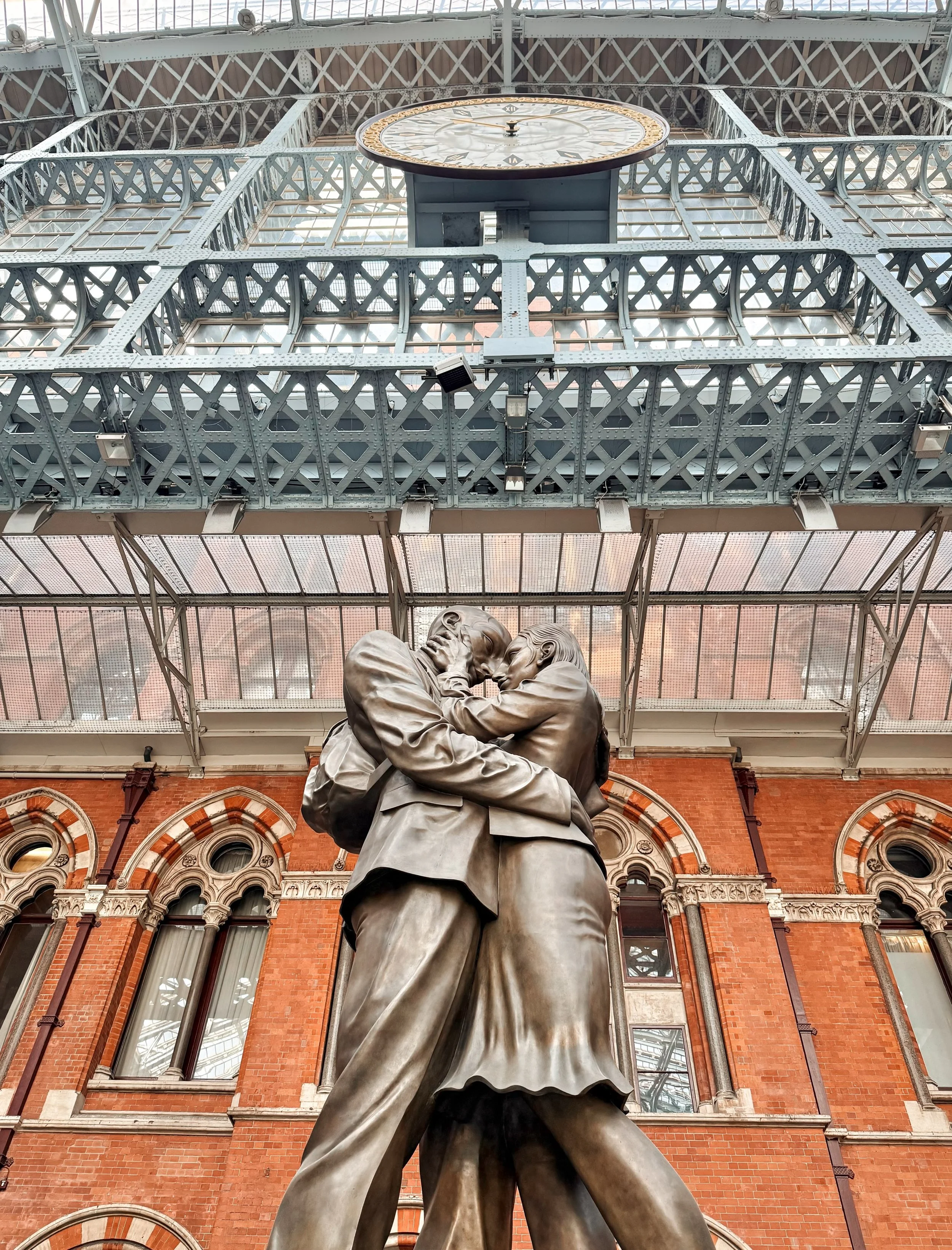 Officially titled The Meeting Place, the massive 9-metre (30 ft) bronze sculpture standing beneath the iconic train shed clock at London&rsquo;s St Pancras International captures an embrace between a couple. 

Designed by British sculptor Paul Day an