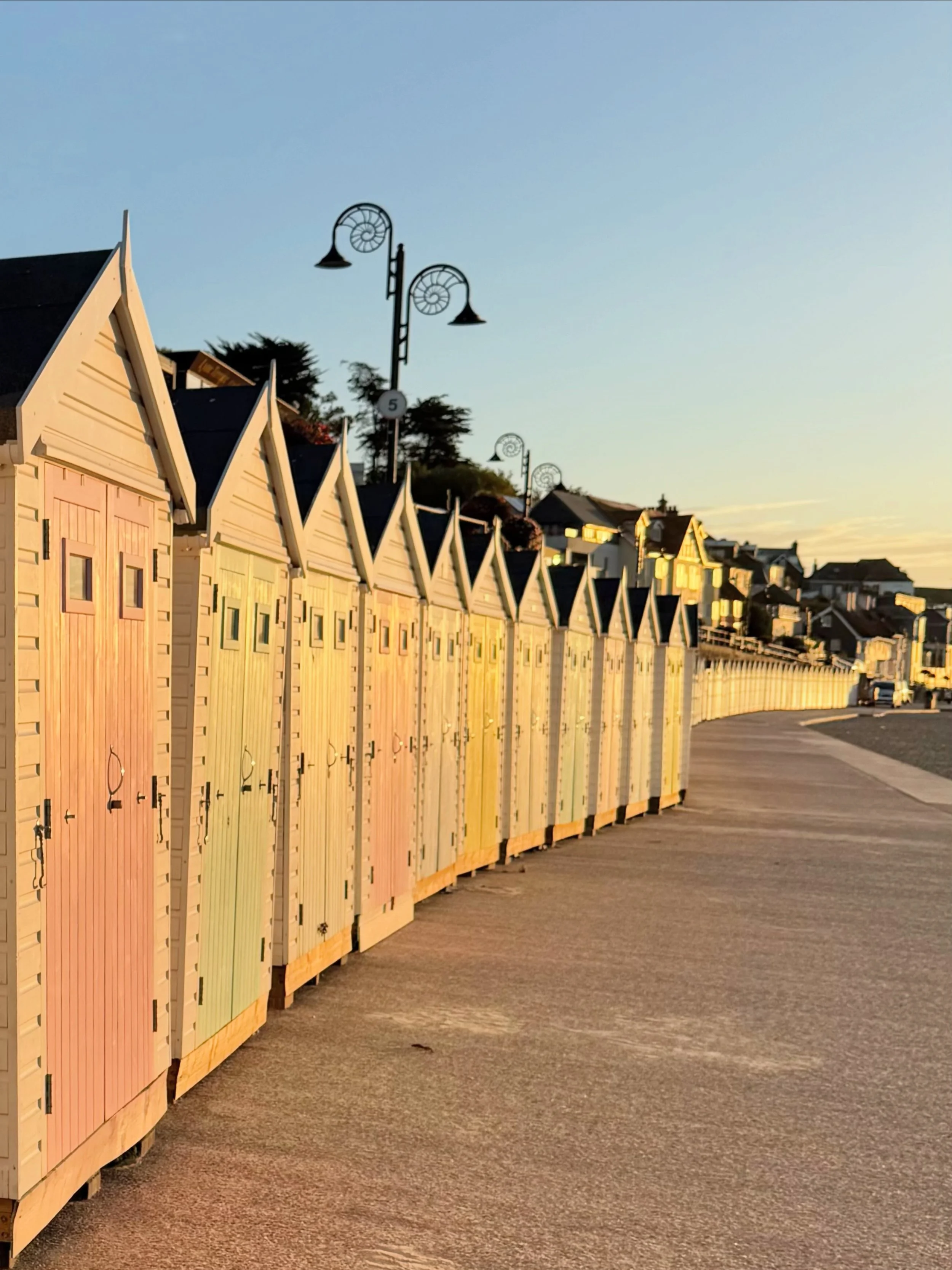Early morning sunlight illuminates the pastel coloured beach huts on Lyme Regis promenade