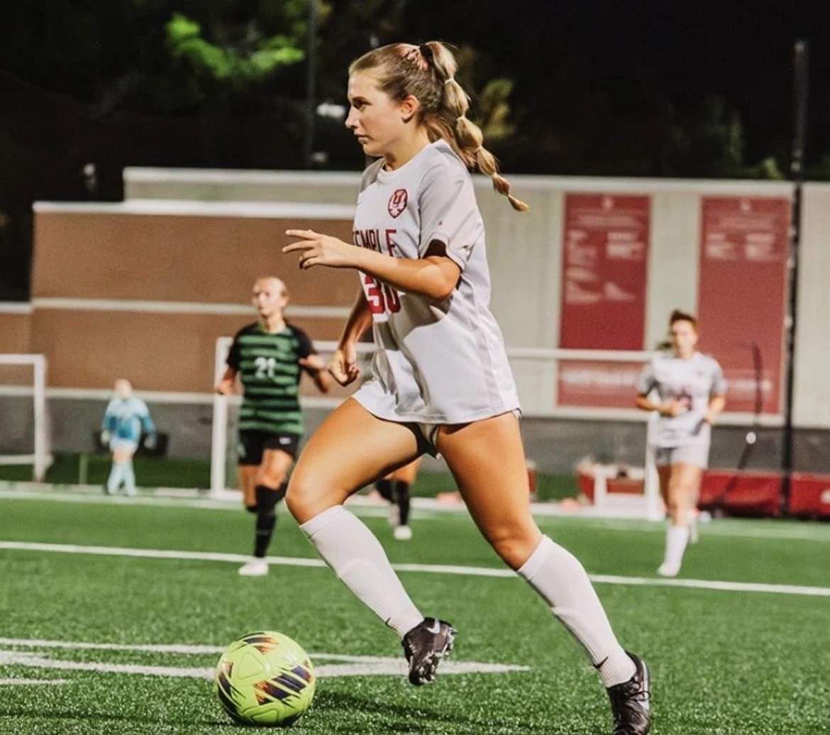 A female soccer player in a blue uniform is on a soccer field, preparing to kick a soccer ball.