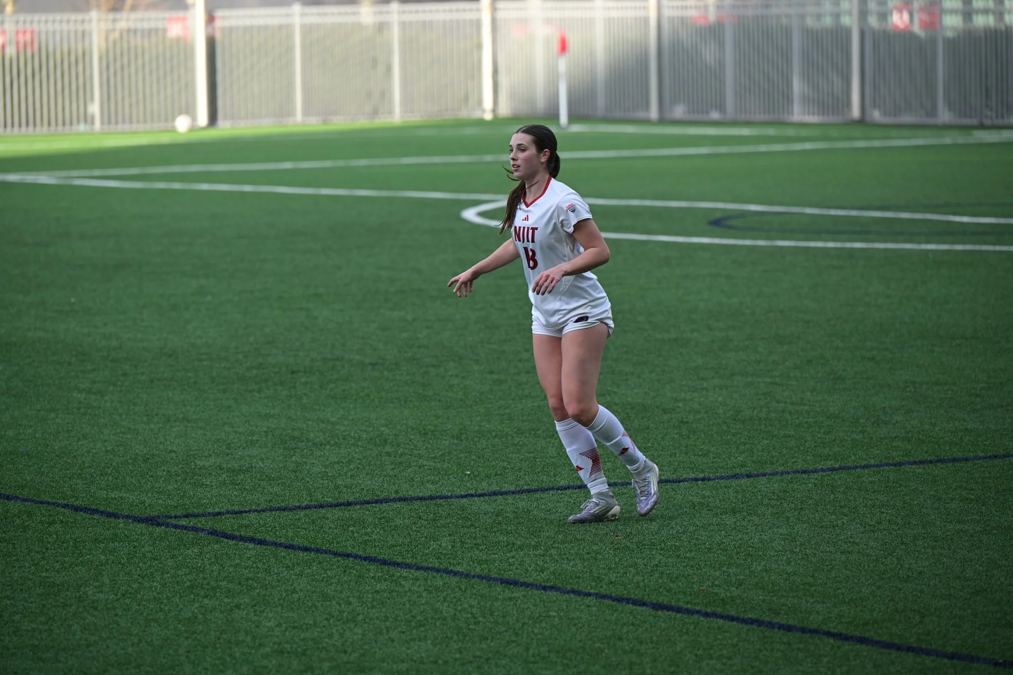 Soccer players, one in a white jersey and one in a blue jersey, compete for the ball on a night game