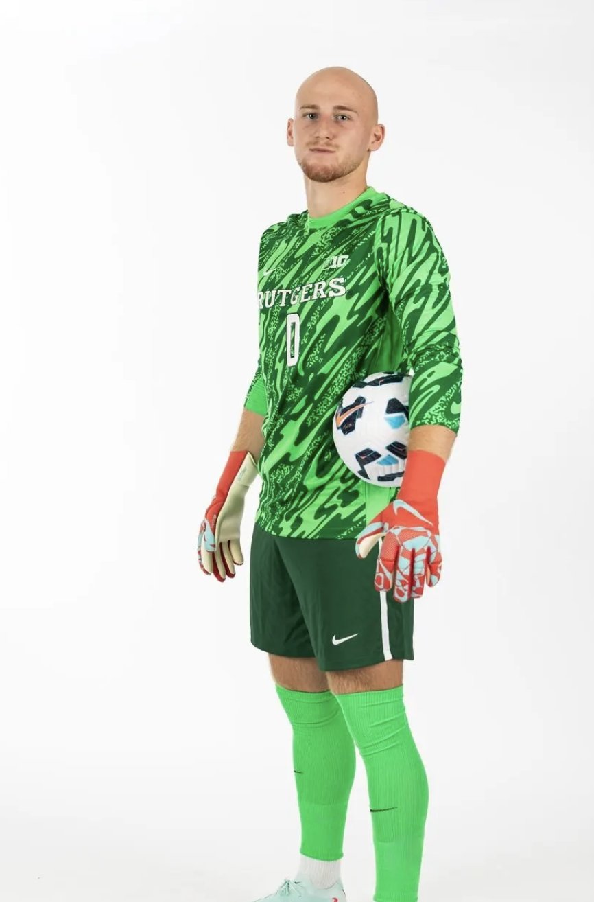 Soccer players standing on a field at night, wearing team jerseys, with one in a blue goalkeeper uniform and others in red jerseys.