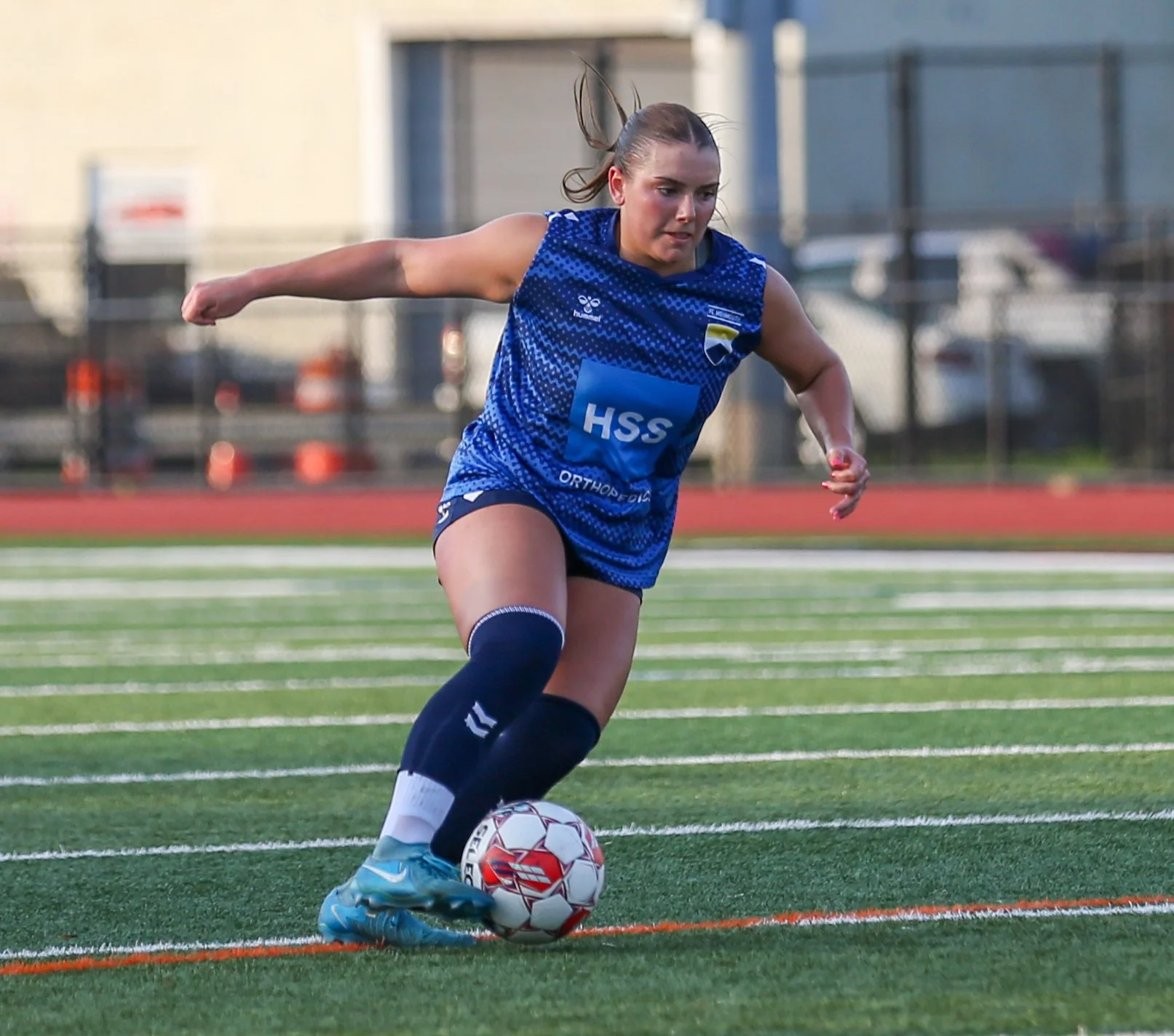 A female soccer player in a blue uniform dribbling a soccer ball on a field.