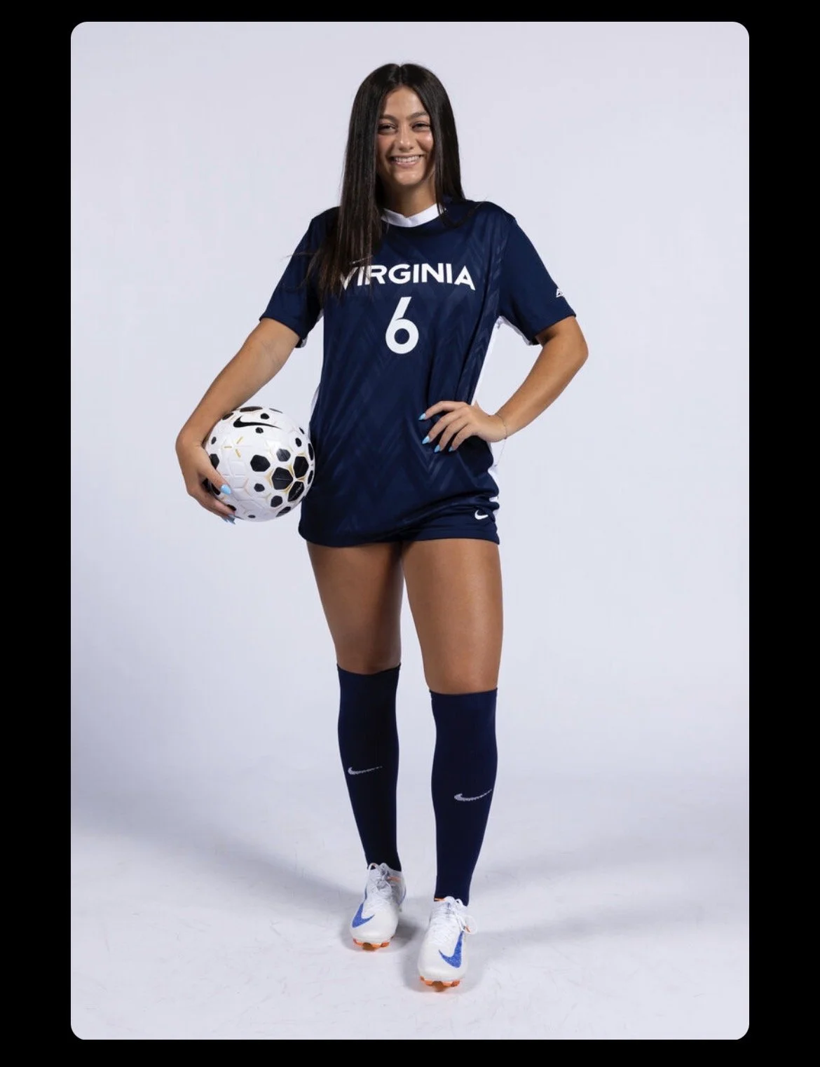 A female soccer player in a blue uniform kicking a soccer ball on the field.