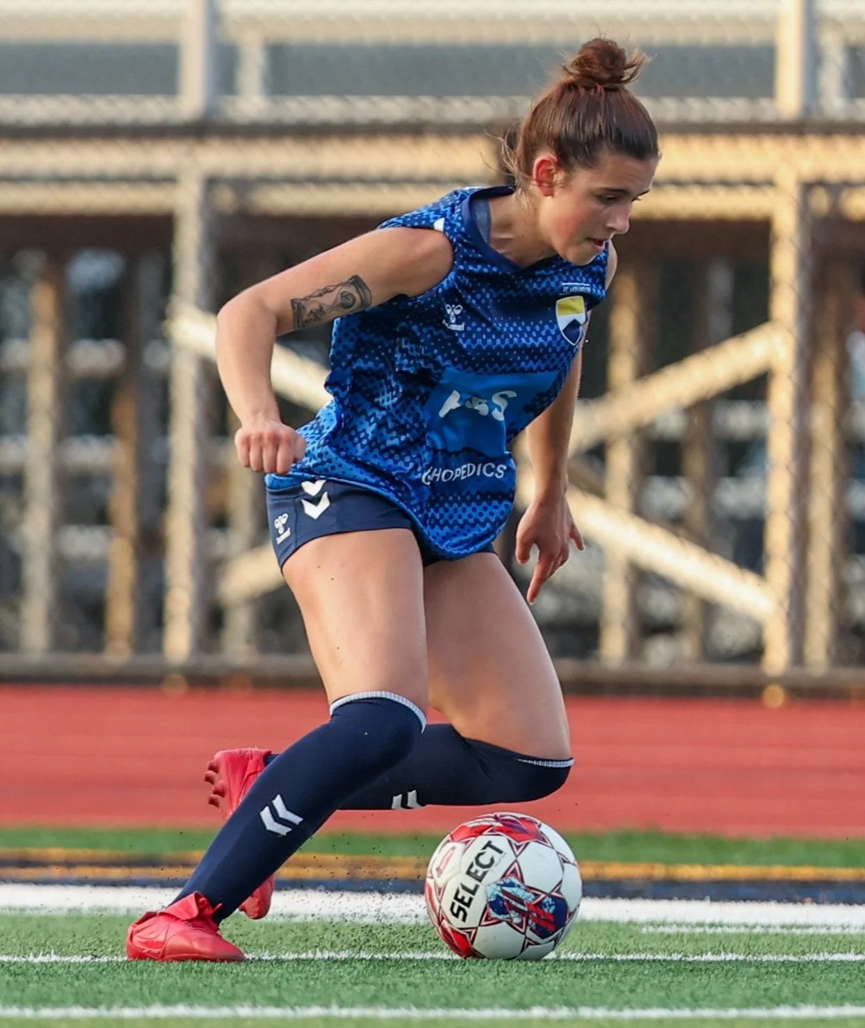 A female soccer player in blue uniform kicks a soccer ball on a field.