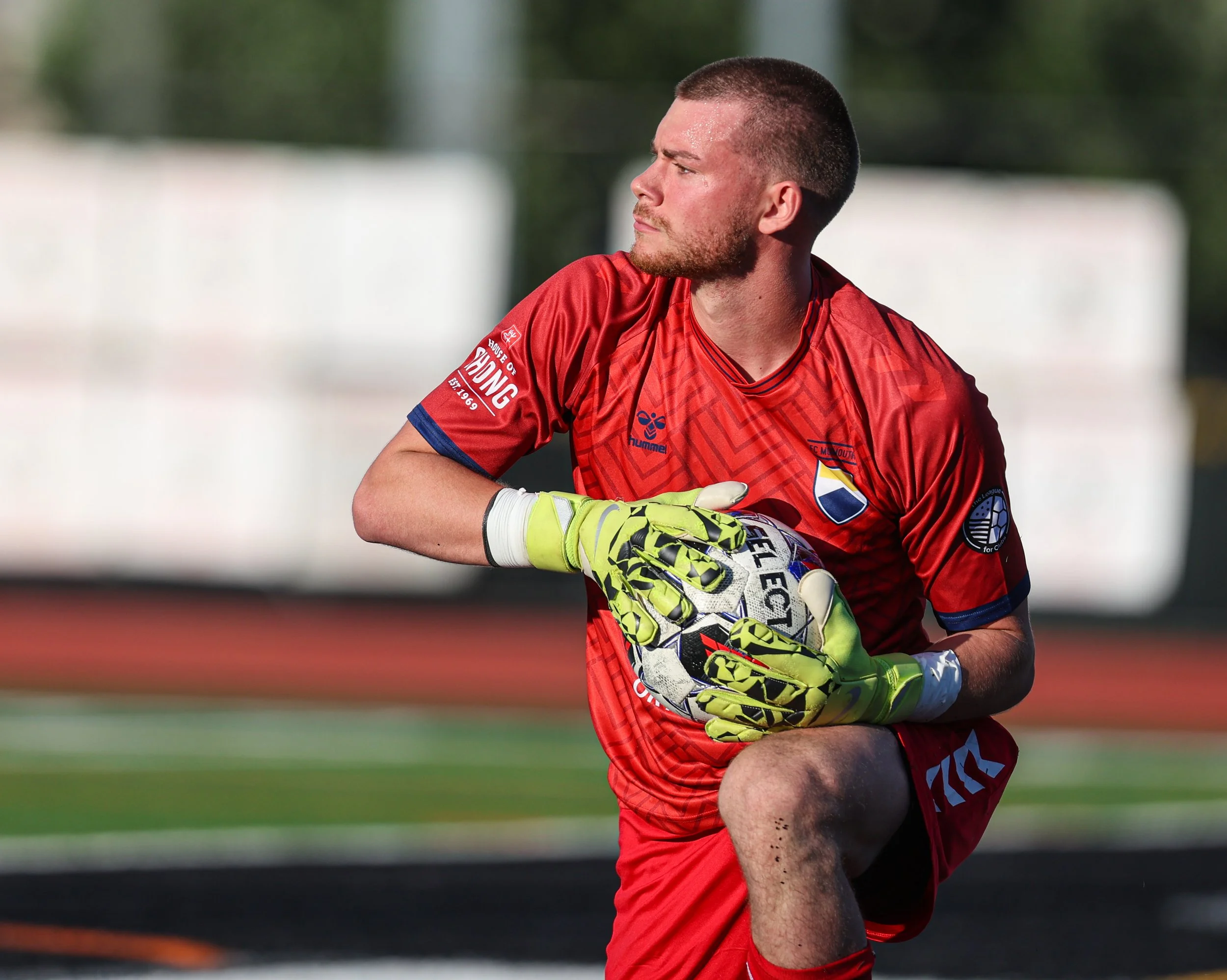 A soccer goalie in a red uniform holding a soccer ball during a game.