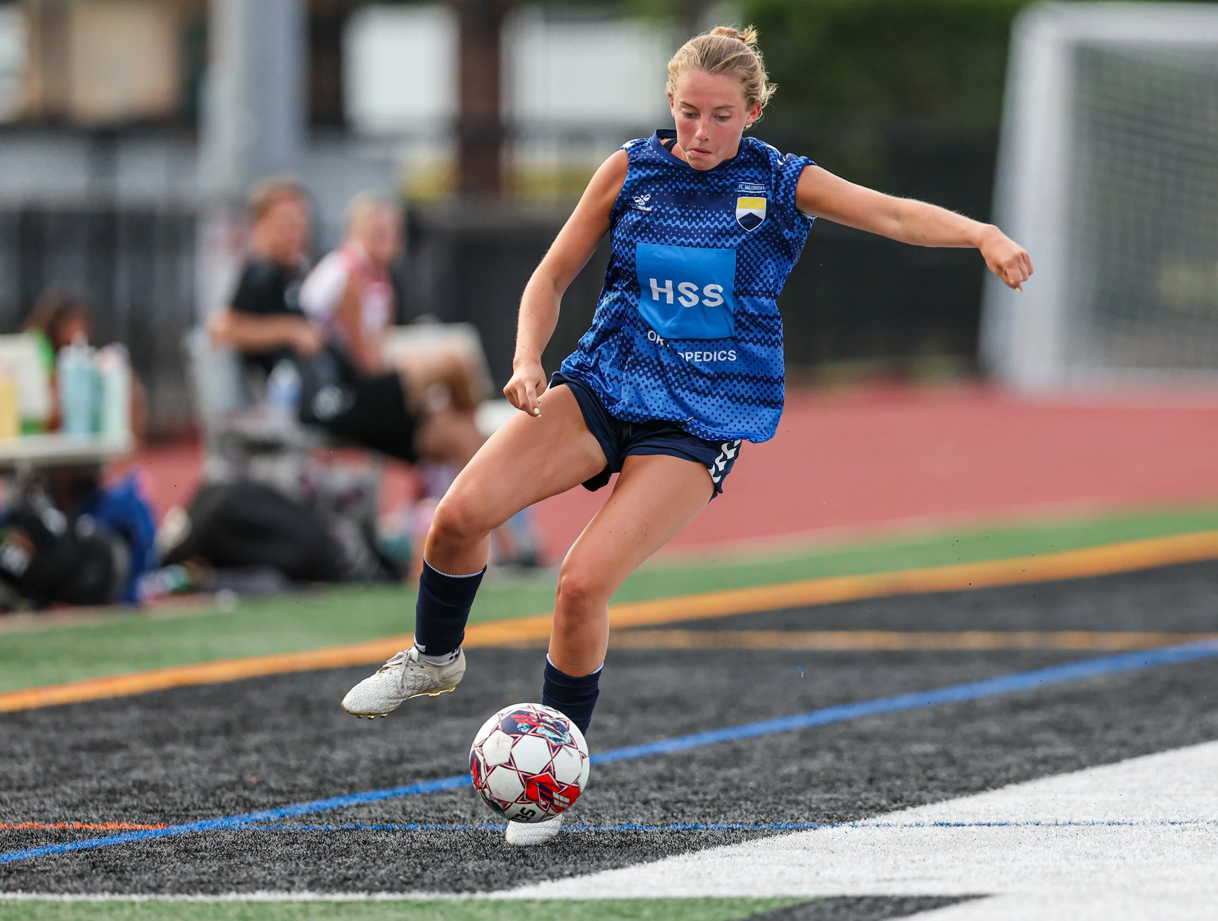 A female soccer player in a blue uniform kicking a soccer ball on the field.