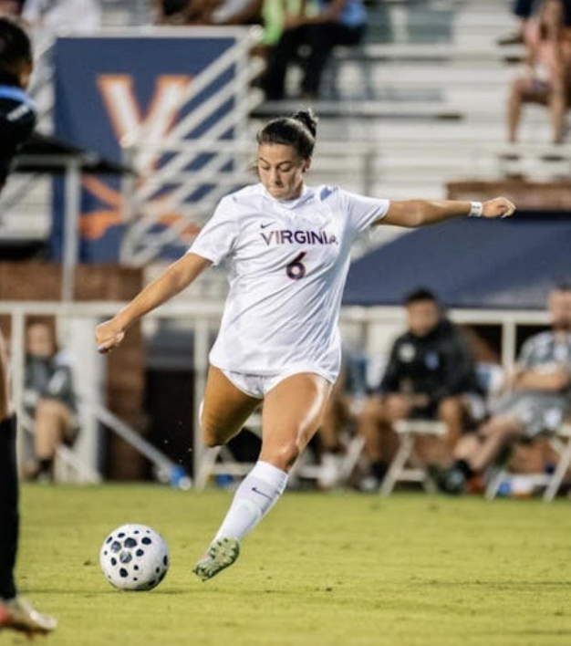 A female soccer player in a blue uniform kicking a soccer ball on the field.