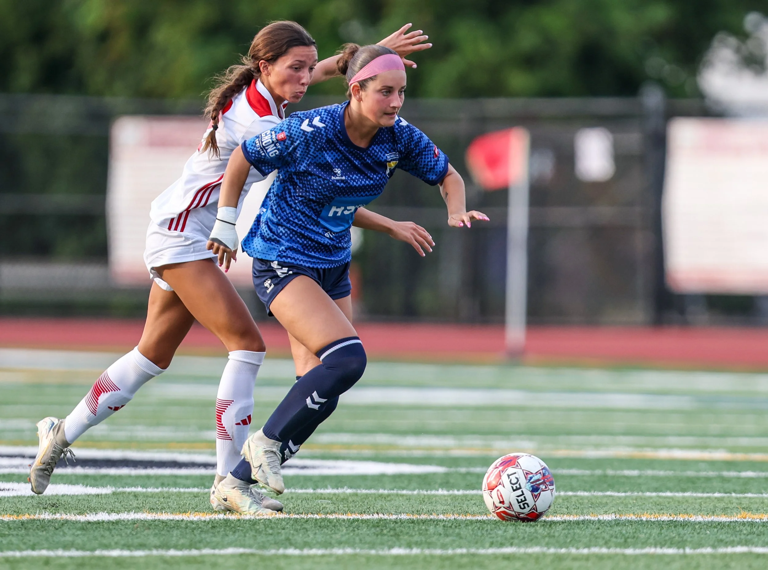 Two female soccer players competing for the ball on the field during a game.