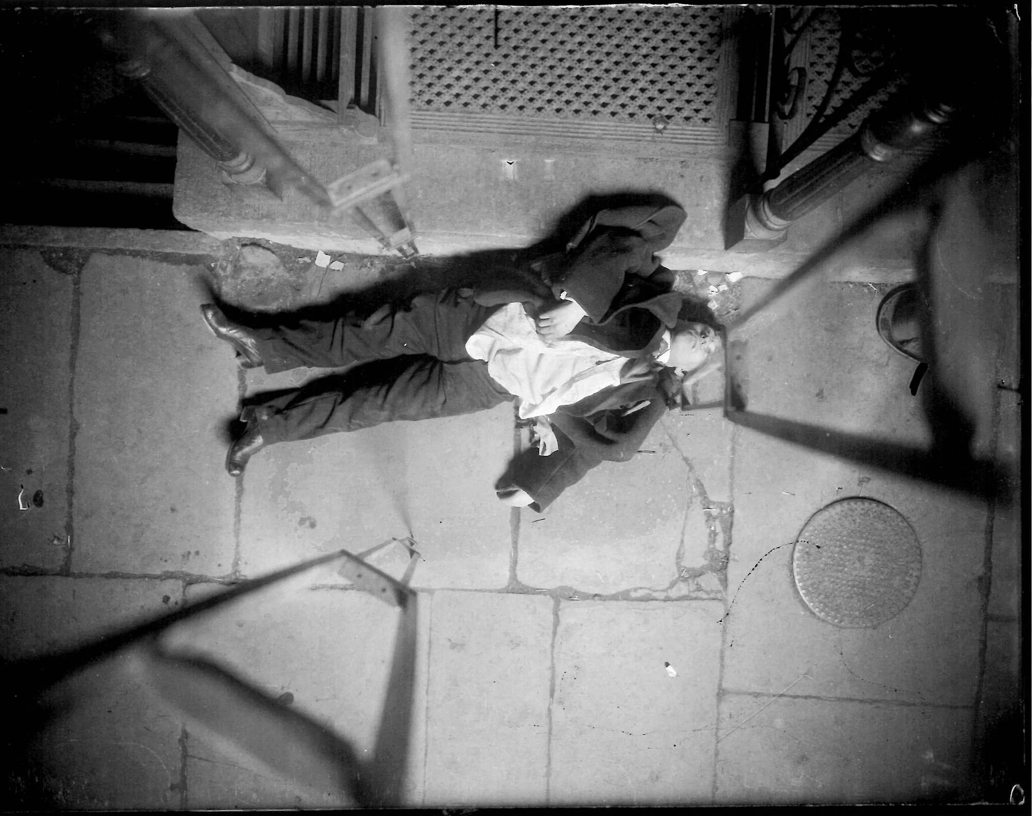 His hat lying where it fell upon his collapse, our victim lies on the sidewalk by the stoop of a café. The photographer's tripod legs complete the surrealistic tableau. 