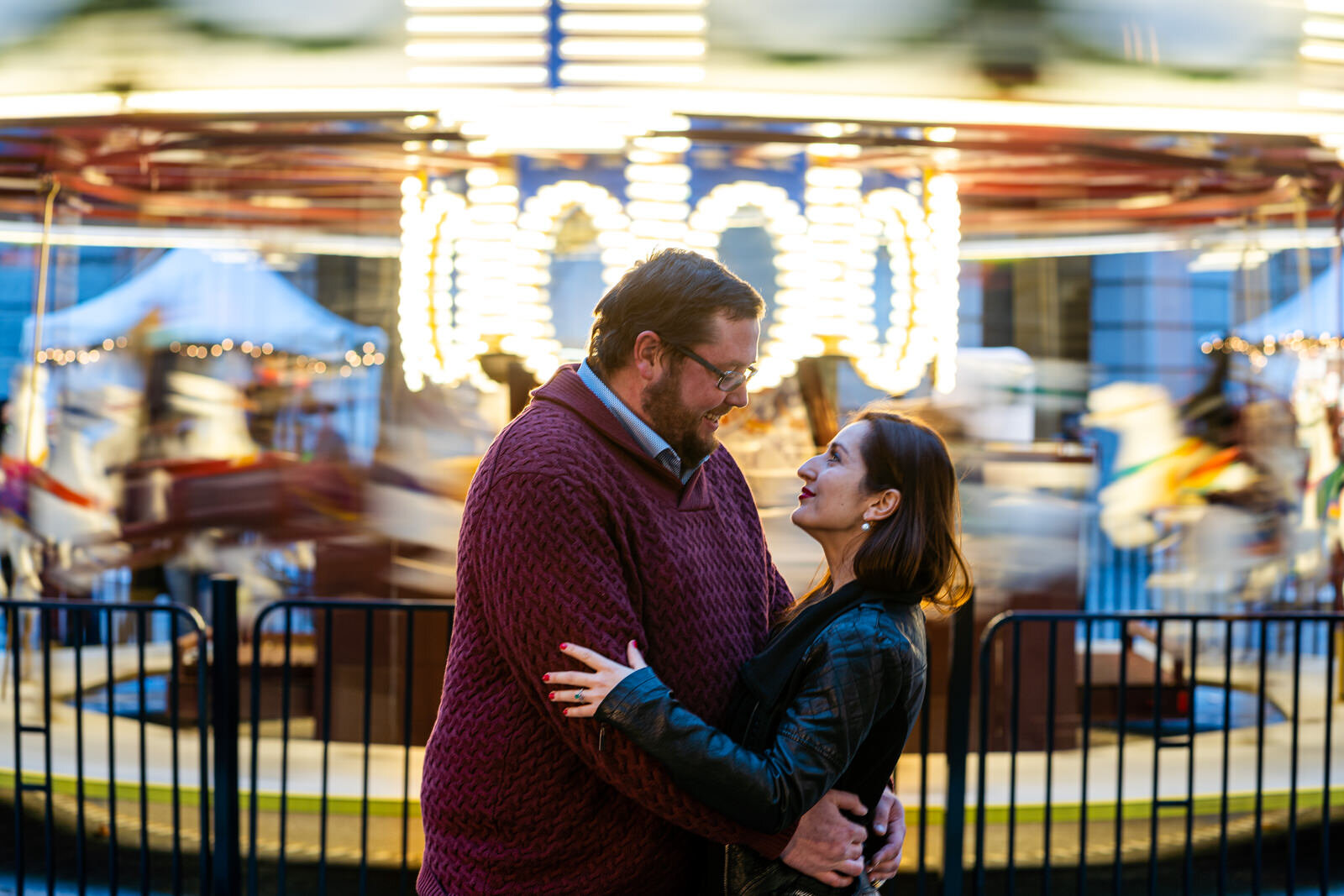 An engaged couple hug each other in front of a carousel in Philadelphia PA