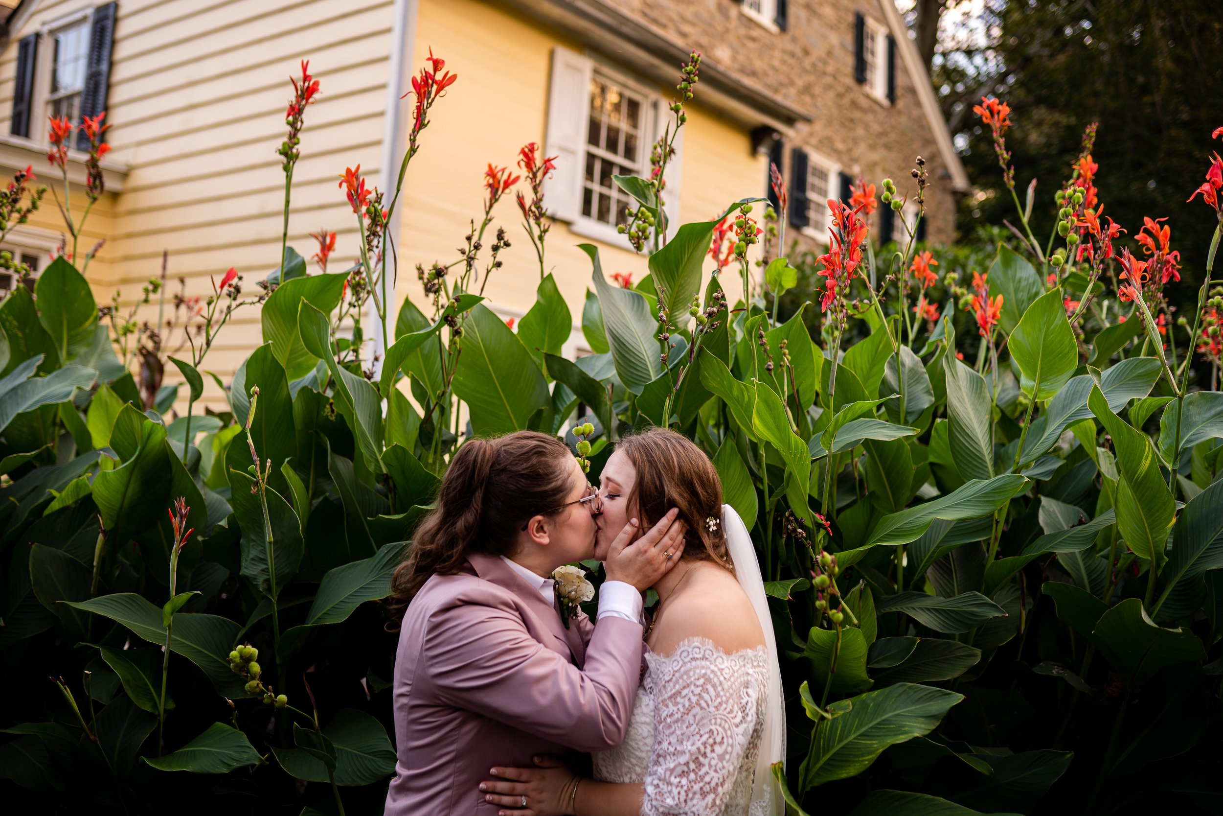Two brides kissing in front of flowers at Ridgeland Mansion in Fairmount Park