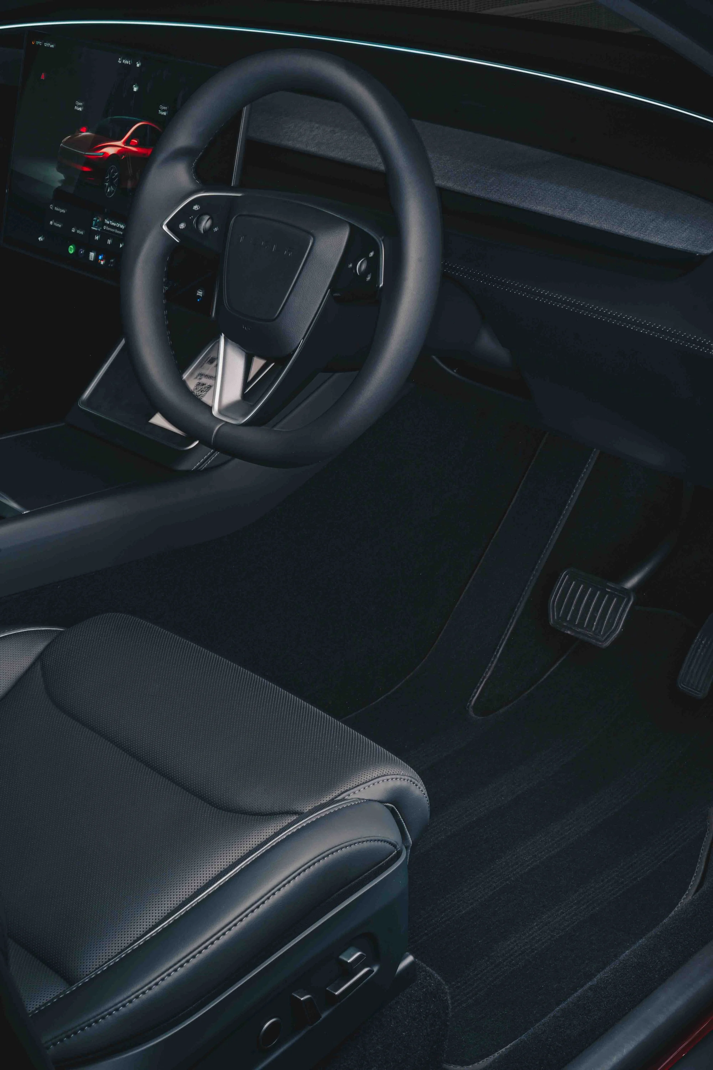 Interior of a Tesla vehicle showing the steering wheel, digital dashboard display, and black leather seats.