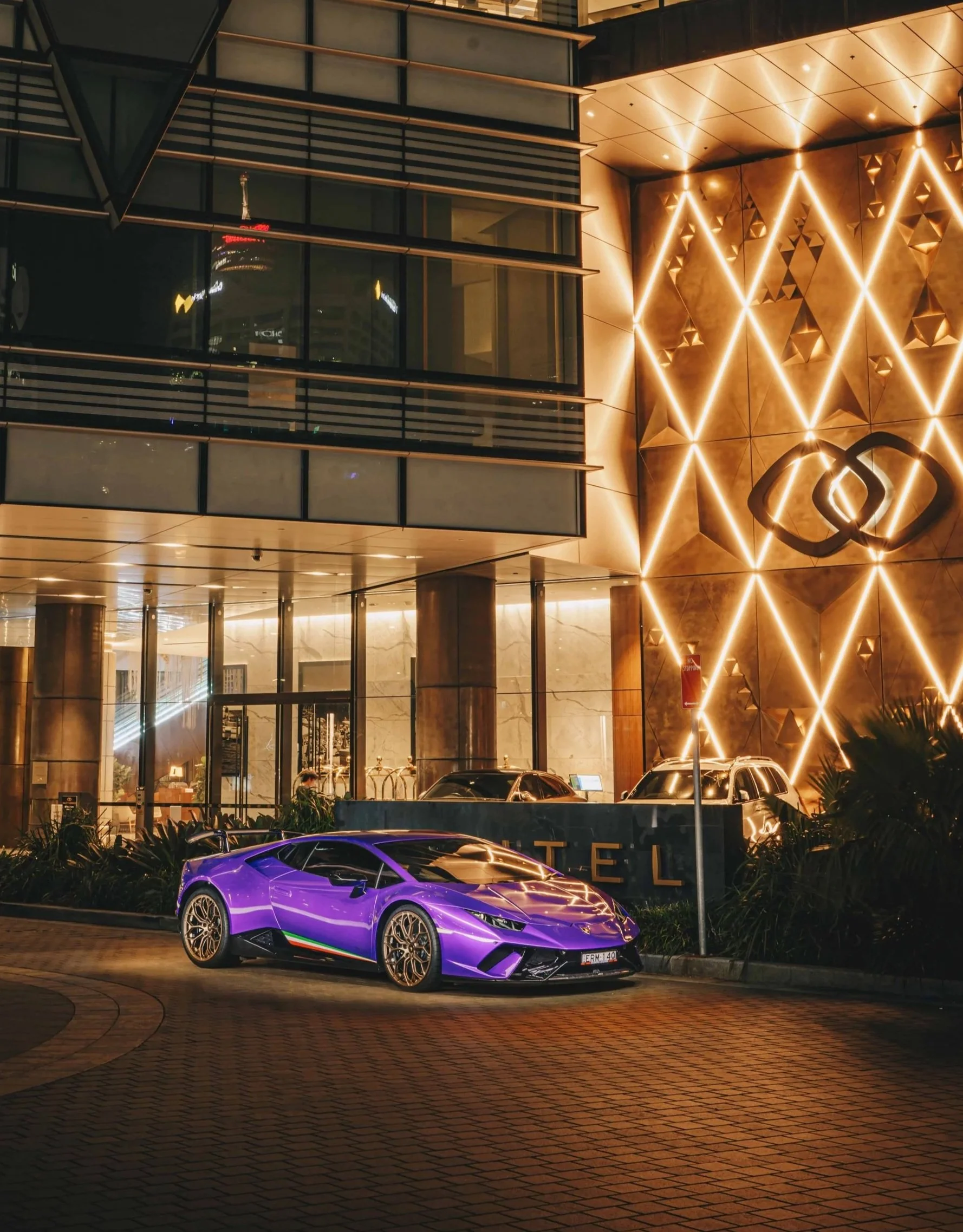Shibbi Car Detail mobile detailing night photography of a glossy purple Lamborghini Huracan parked on a city street illuminated by golden and blue city lights Sydney.
