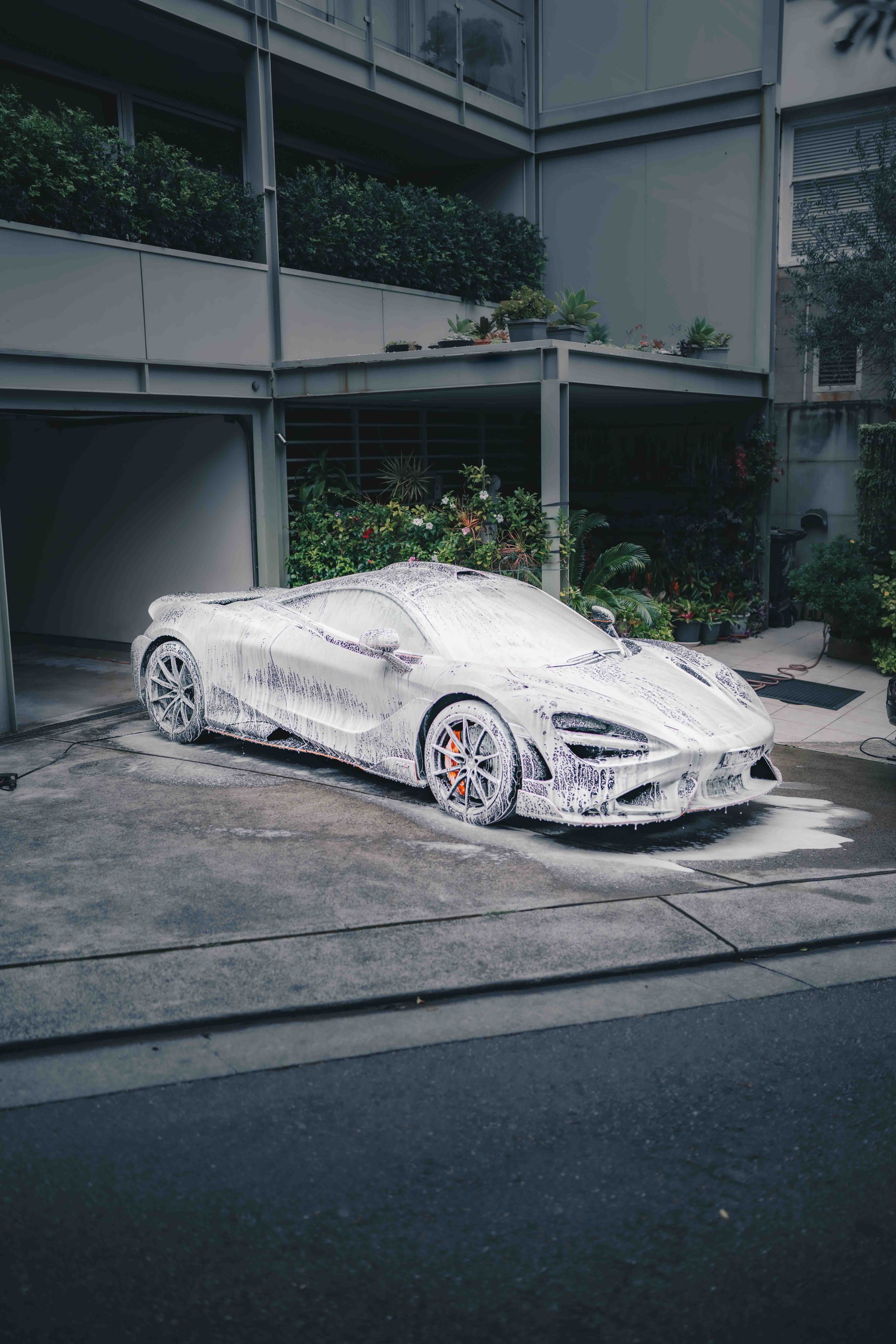 Shibbi Car Detail mobile car detailing applying thick snow foam from a foam cannon onto a McLaren 765LT for a touchless pre-wash in a customer's driveway in vaucluse, Sydney.