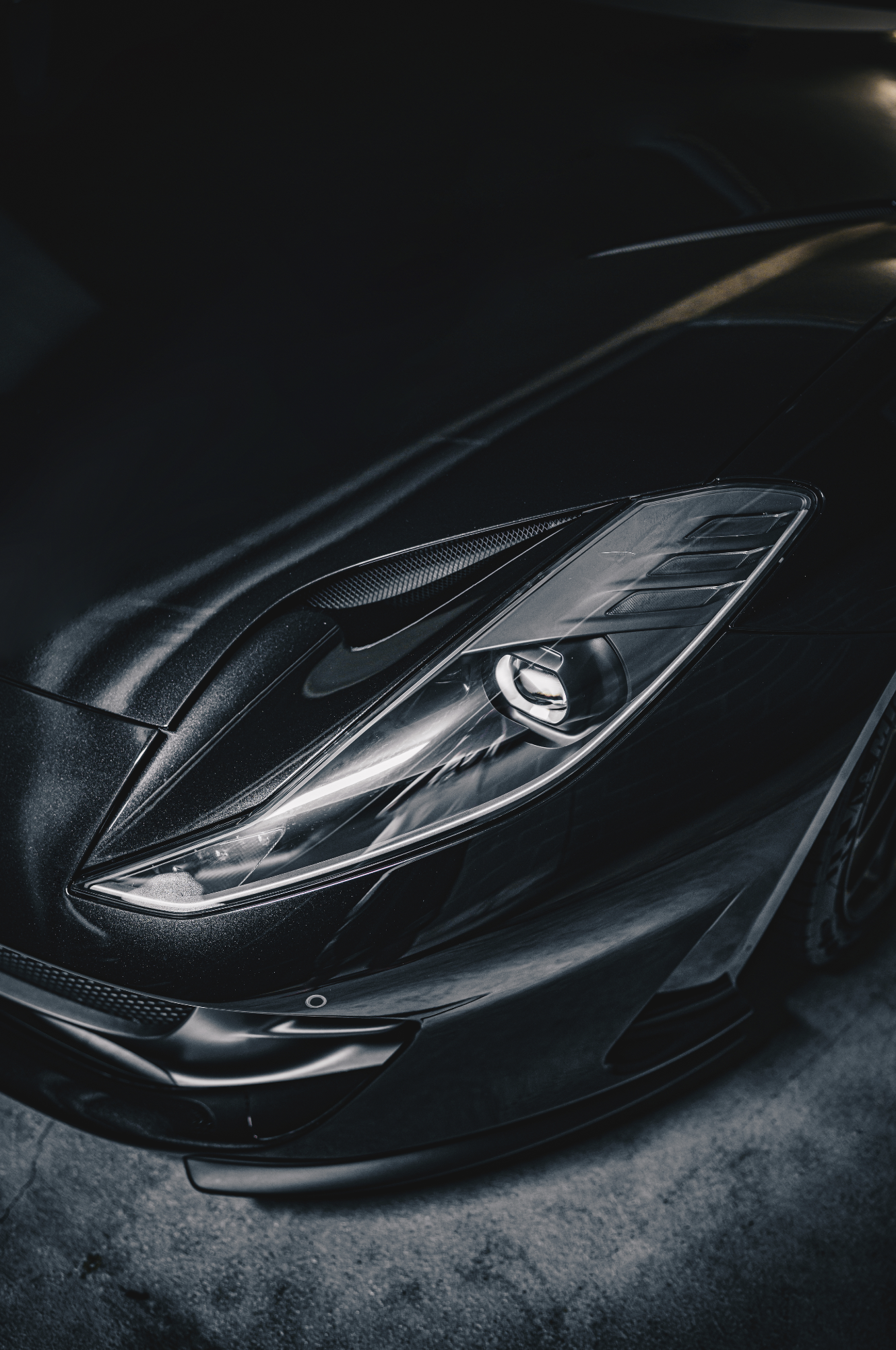 Close-up of the front part of a black luxury sports car, showing the headlight, sleek design, and a portion of the hood.