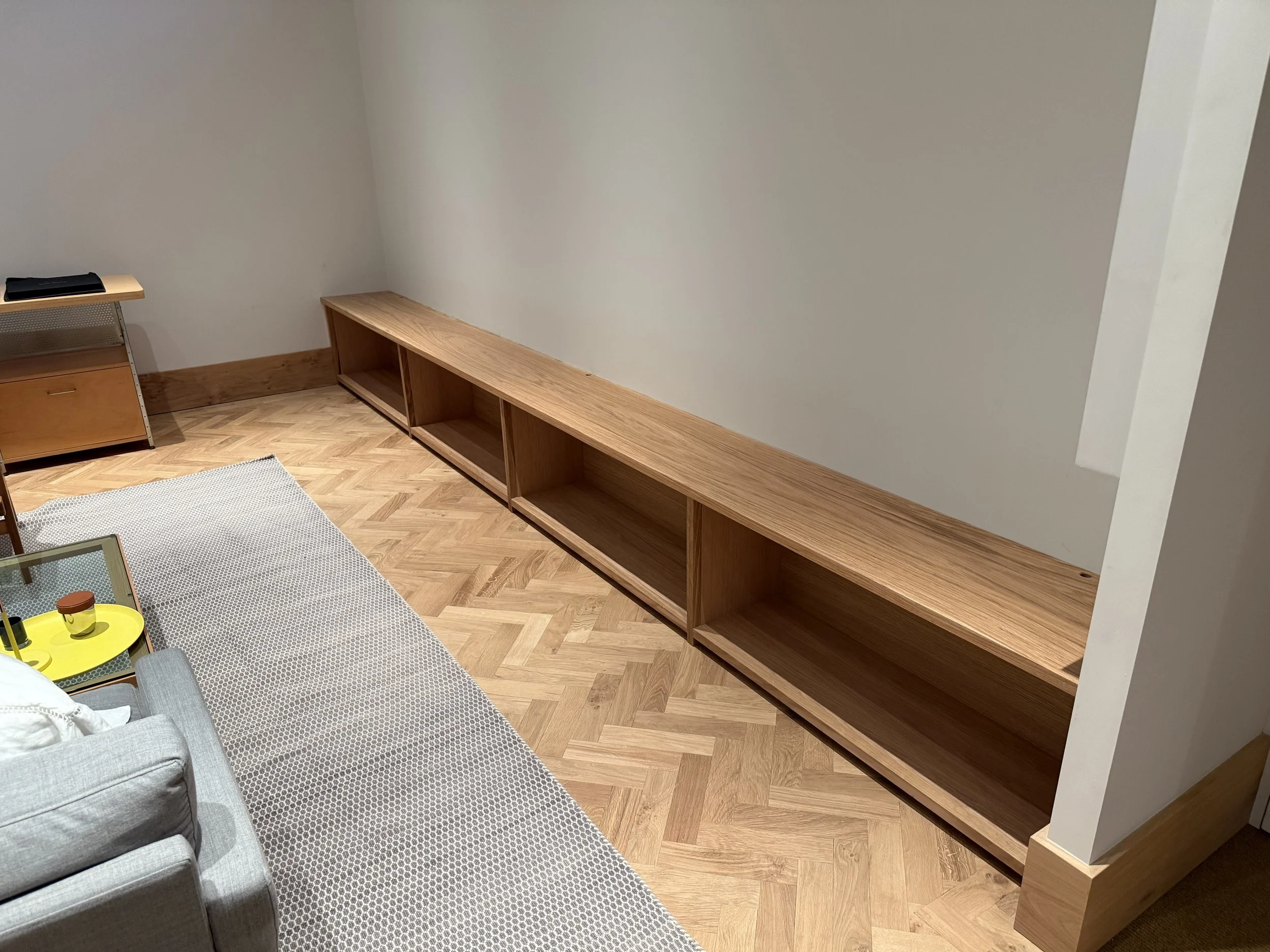 Close-up of oak display base with subtle shadow gap and herringbone timber floor in London living room.