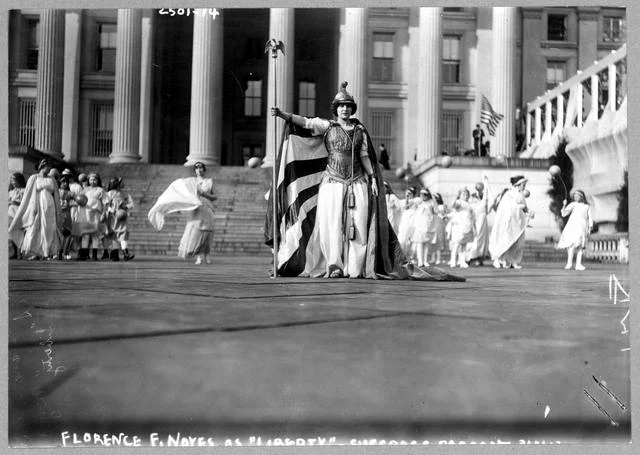 German actress Hedwig Reicher wearing costume of "Columbia" with other suffrage pageant participants standing in background in front of the Treasury Building, March 3, 1913, Washington, D.C