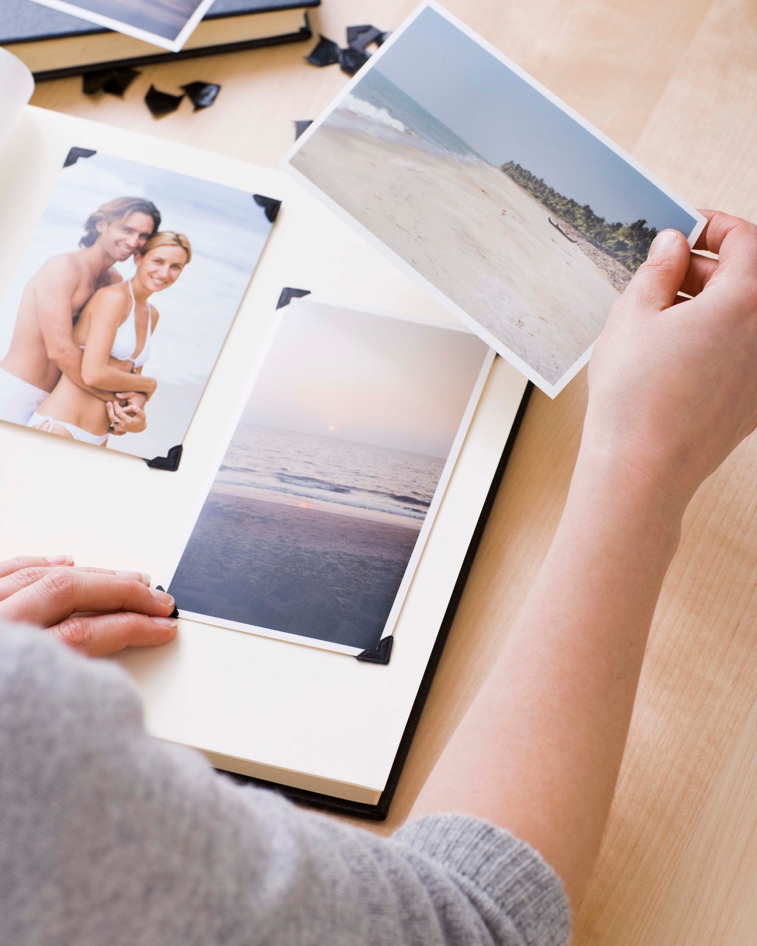 Person flipping through a photo album with beach and ocean pictures and a couple's photo on a sandy beach.