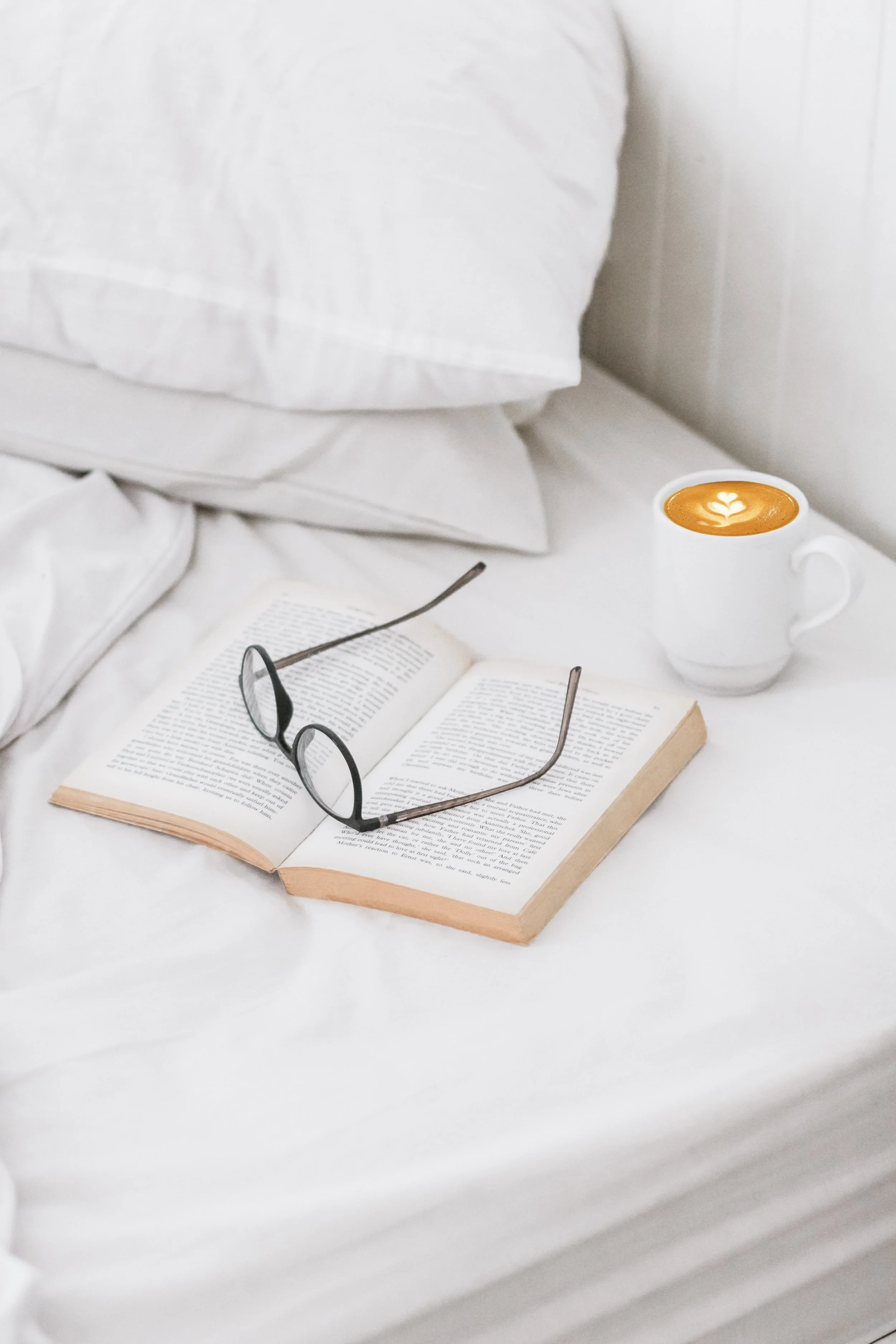 A bed with a coffee, book and pair on glasses