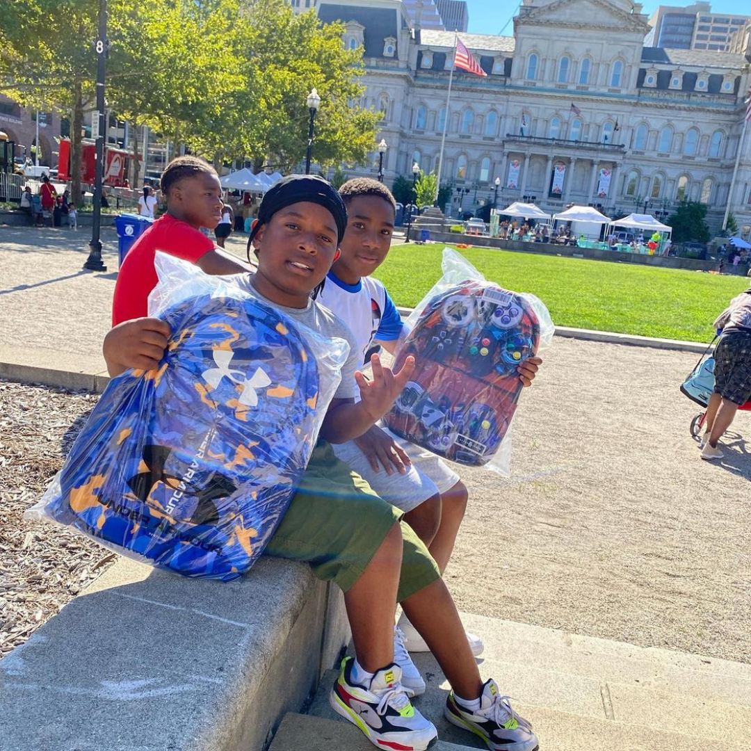 Image of two children holding up new backpacks from the Back to School event