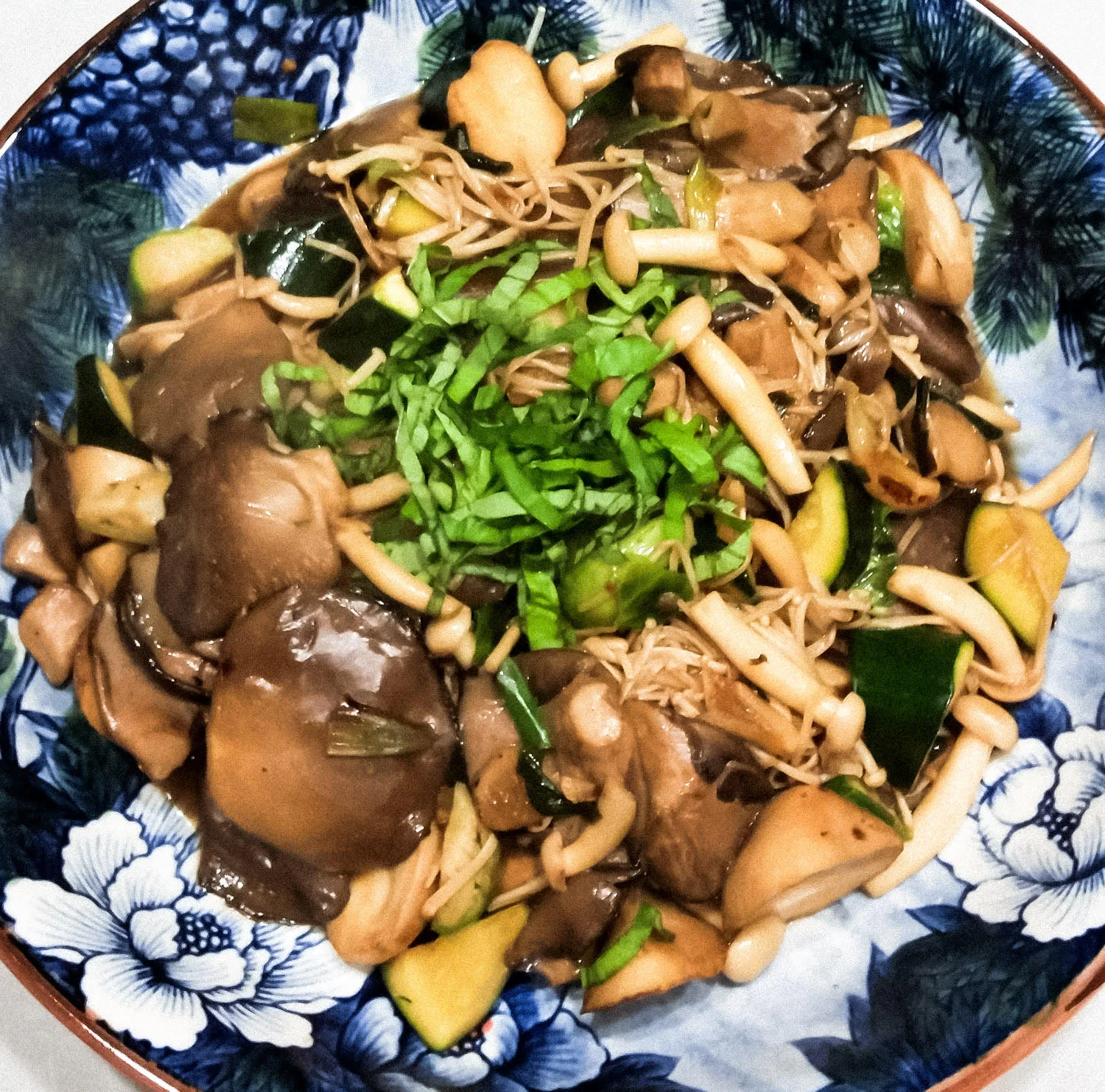 In serving bowl, Three-Cup Mushrooms with zucchini, topped with basil.
