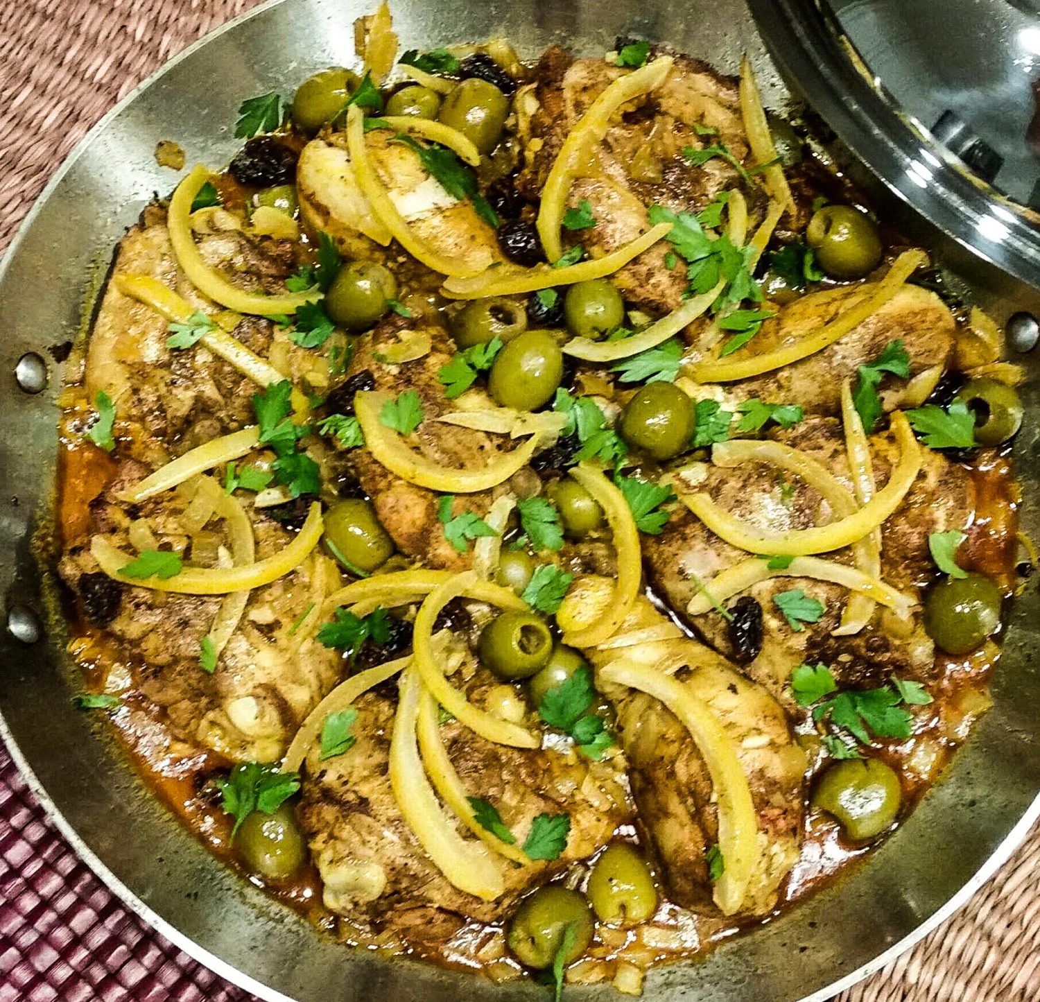 Perfectly cooked chicken thighs and drumsticks nestled in a pan with preserved lemon strips, green olives and raisins.