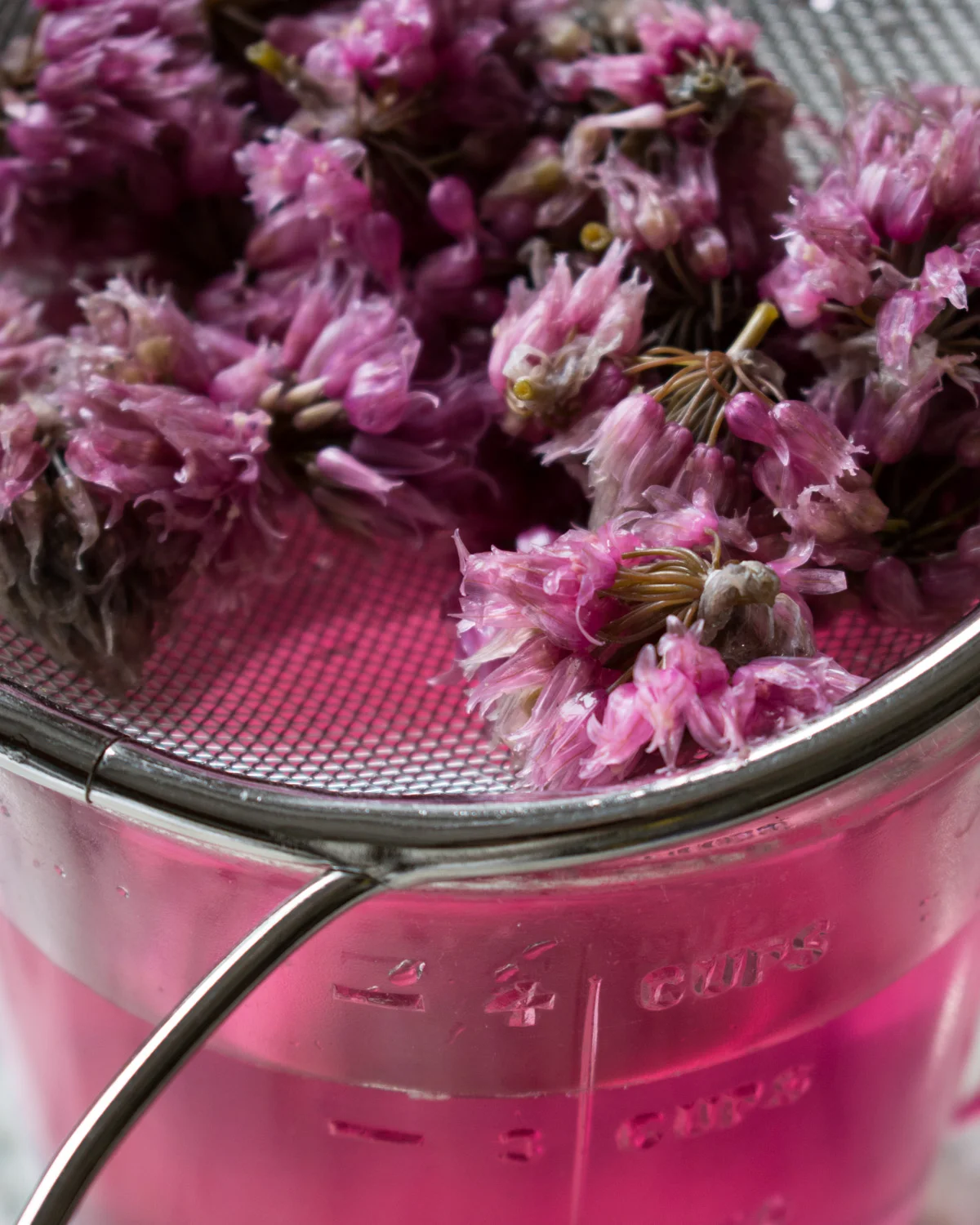 Pouring the chive flower vinegar infusion through a strainer.