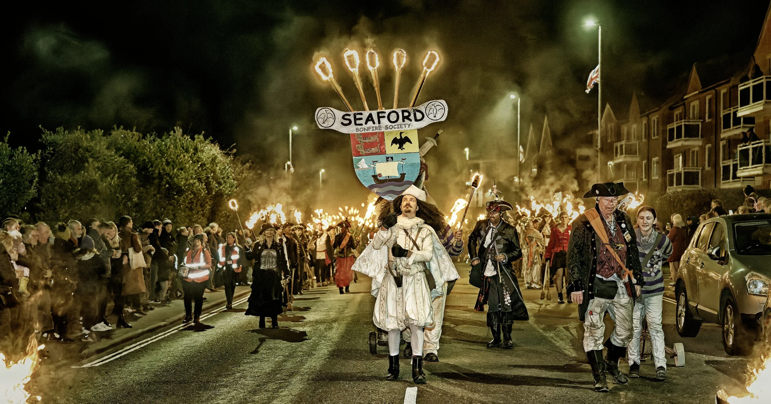 Documentary fieldwork photograph of a Sussex Bonfire Society parade in Seaford, showing the Lord Monteagle with flaming torches