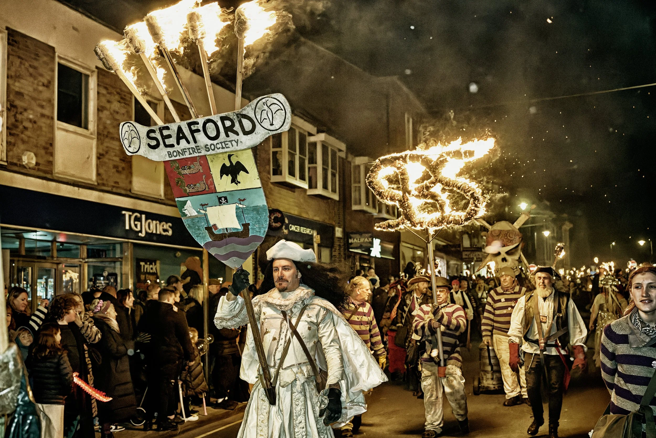 Documentary fieldwork photograph of a Sussex Bonfire Society parade in Seaford, showing the Lord Monteagle and the SBS logo in flames
