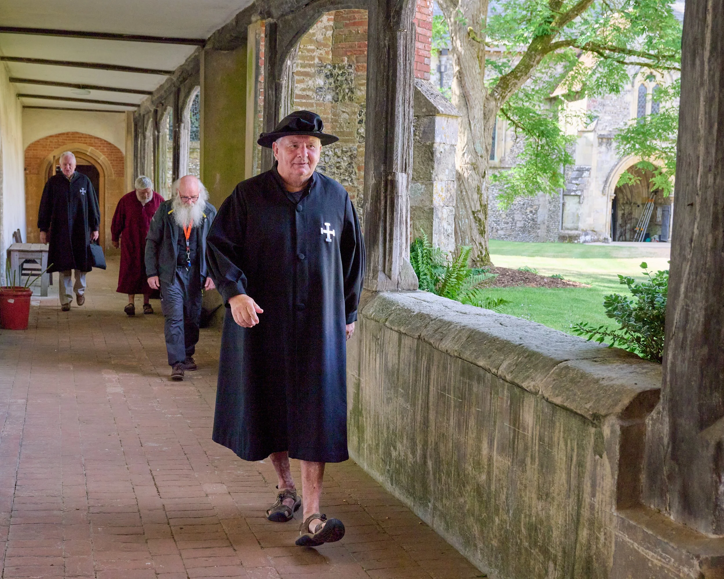 This documentary fieldwork photograph shows traditionally robed Brothers leaving Saint Cross Church via the 16th-century ambulatory after the Matins service.