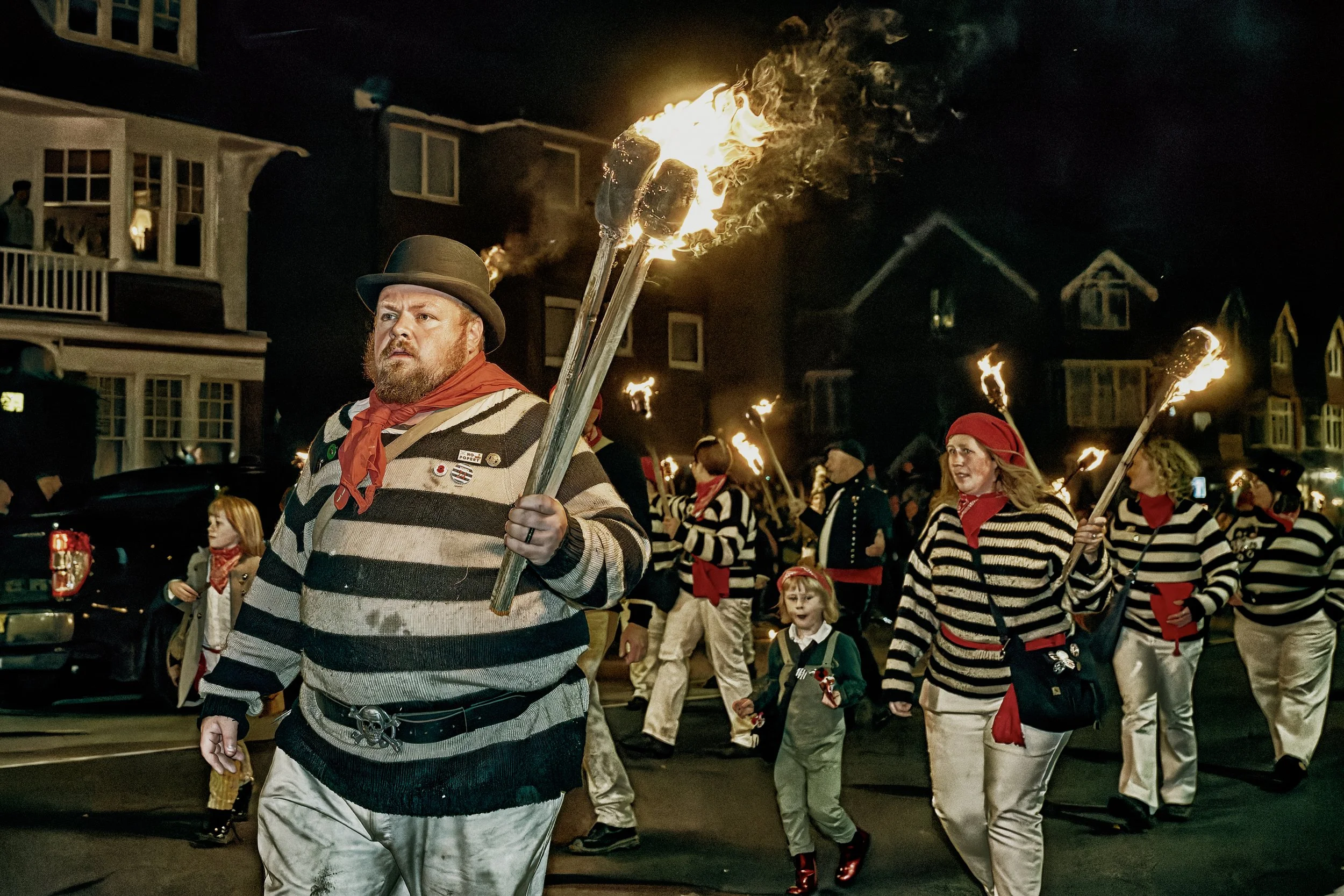 Documentary fieldwork photograph of a Sussex Bonfire Society parade in Seaford, showing the Seaford Shags carrying flaming torches