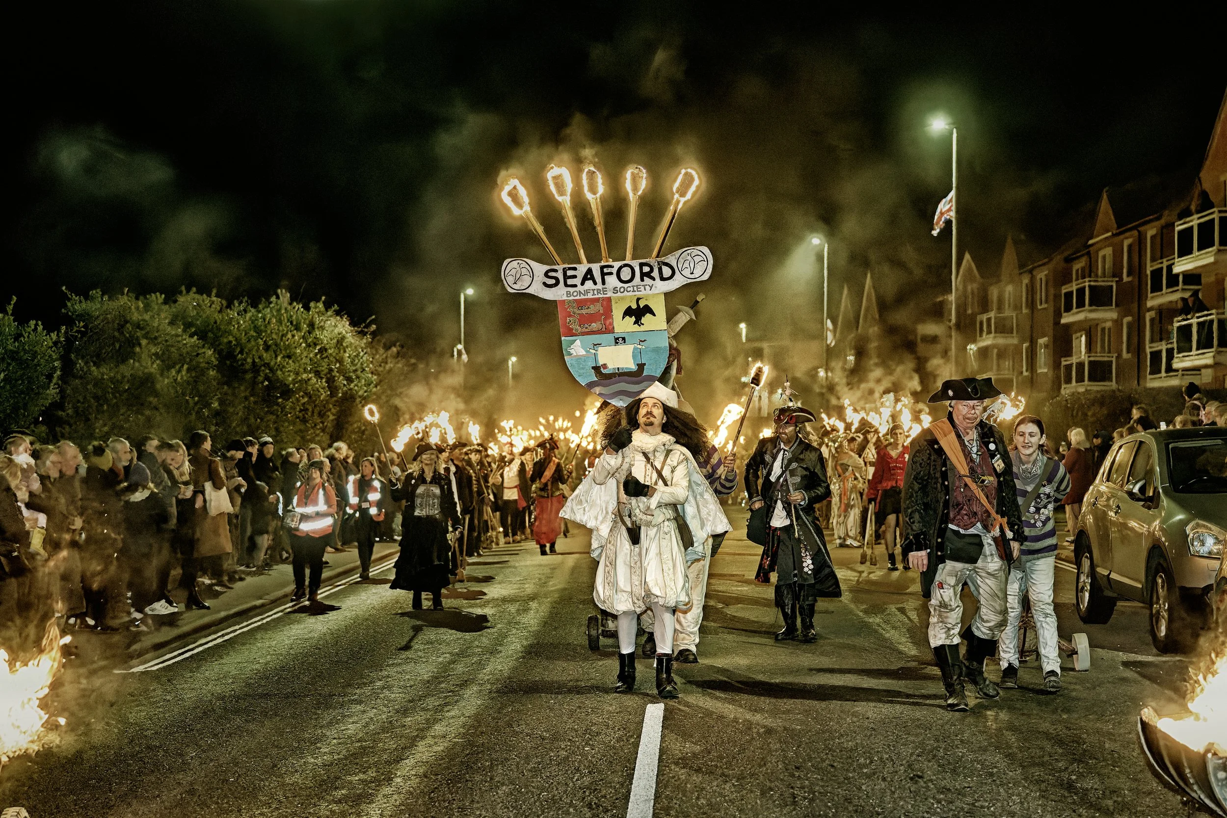 Documentary fieldwork photograph of a Sussex Bonfire Society parade in Seaford, showing the Lord Monteagle with flaming torches