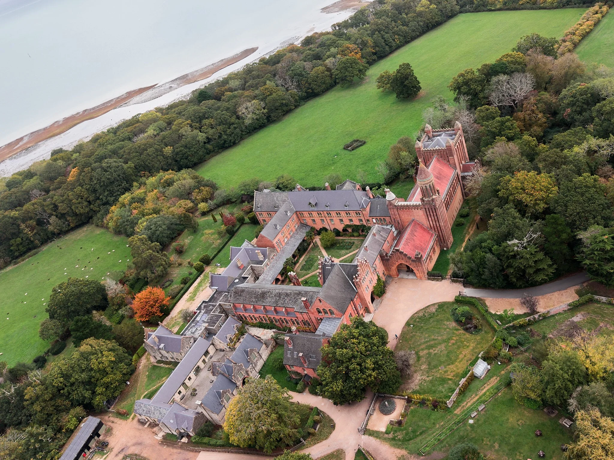 This documentary fieldwork photograph is of Quarr Abbey. A drone photograph depicts the Abbey complex, surrounding land, and its proximity to the Solent shoreline.