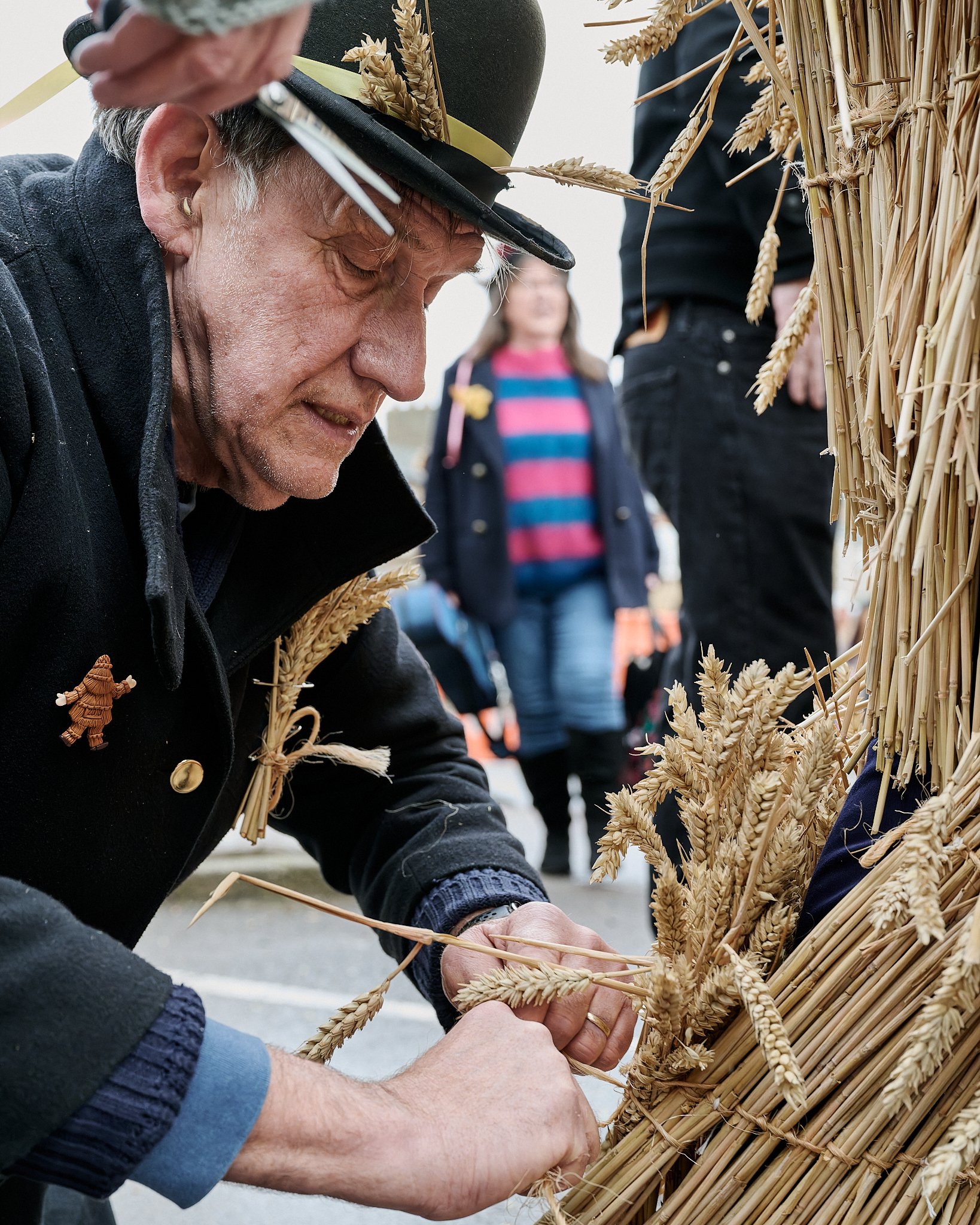 Documentary fieldwork photograph of the Straw Bear and handler in Whittlesea, showing the handler repairing the sraw bear's costume
