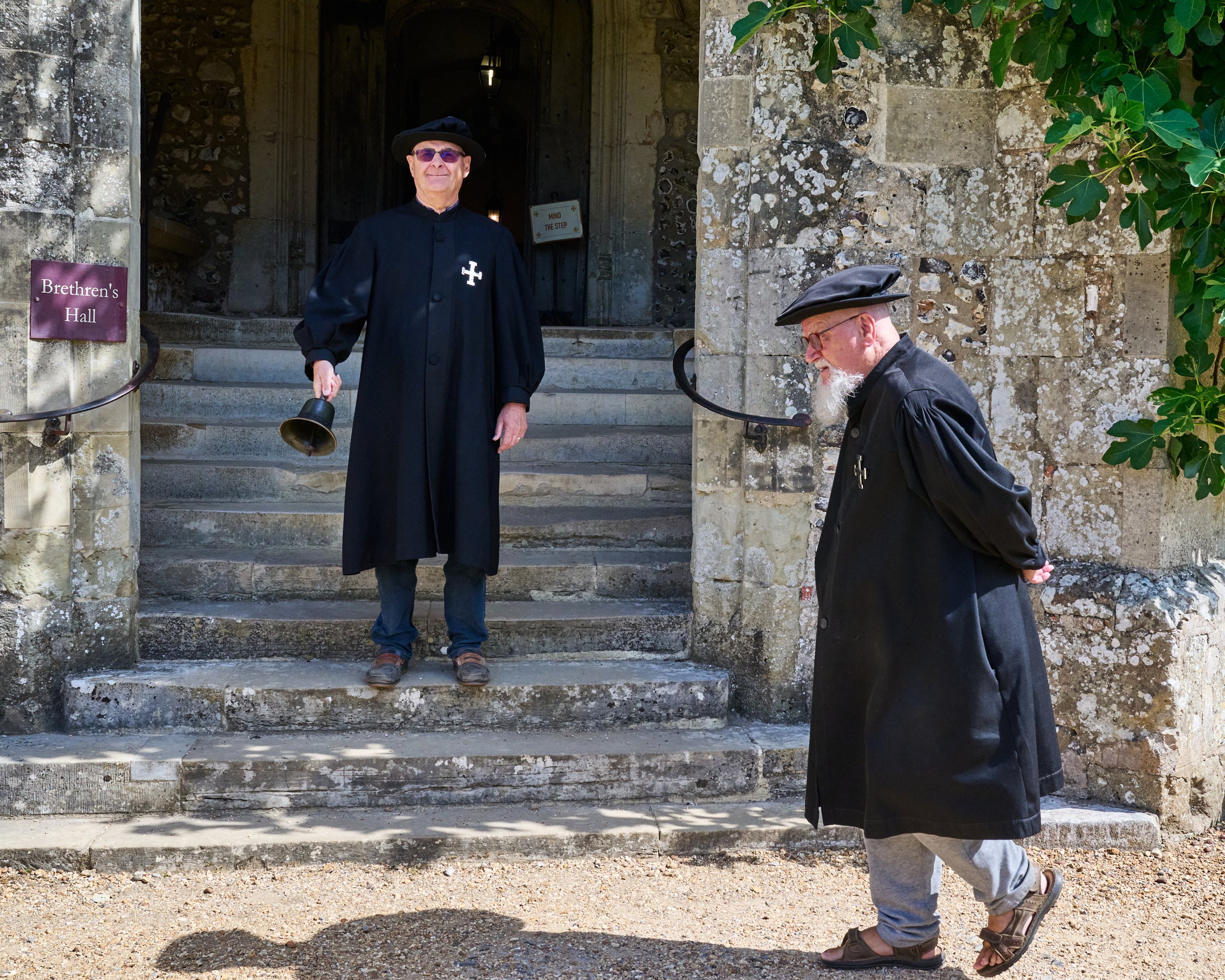 This documentary fieldwork photograph shows a traditionally robed Brother making his way to Pay Parade at the Hospital of Saint Cross before the summoning hand bell.