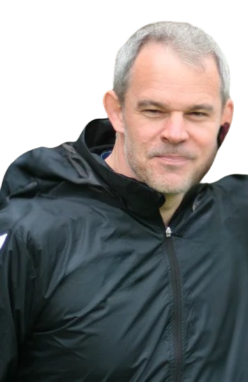 A middle-aged man with short gray hair and a beard, wearing a black jacket, outdoors against a black background.